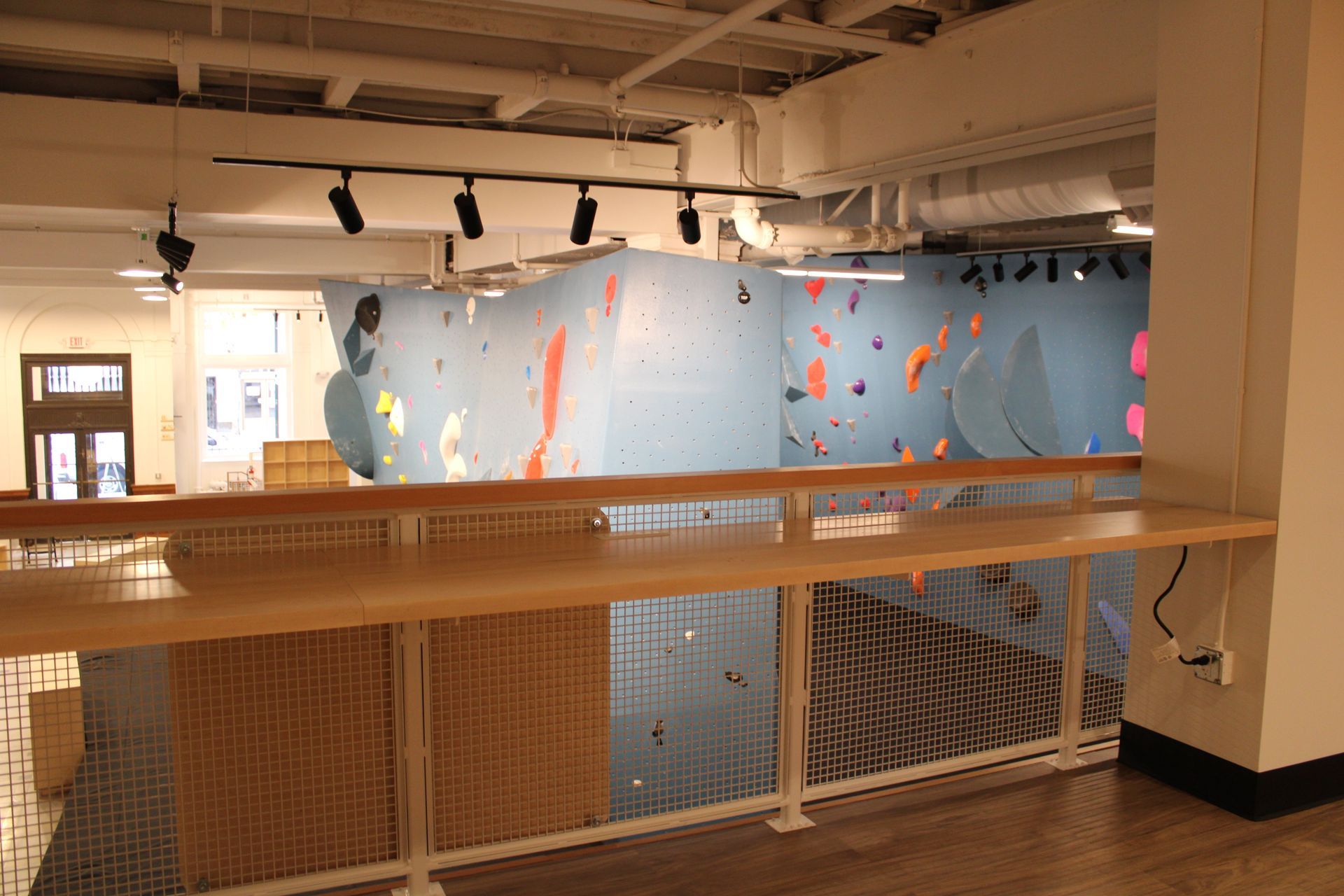 Indoor climbing gym with blue climbing walls and colorful holds. Wooden railing and open view.