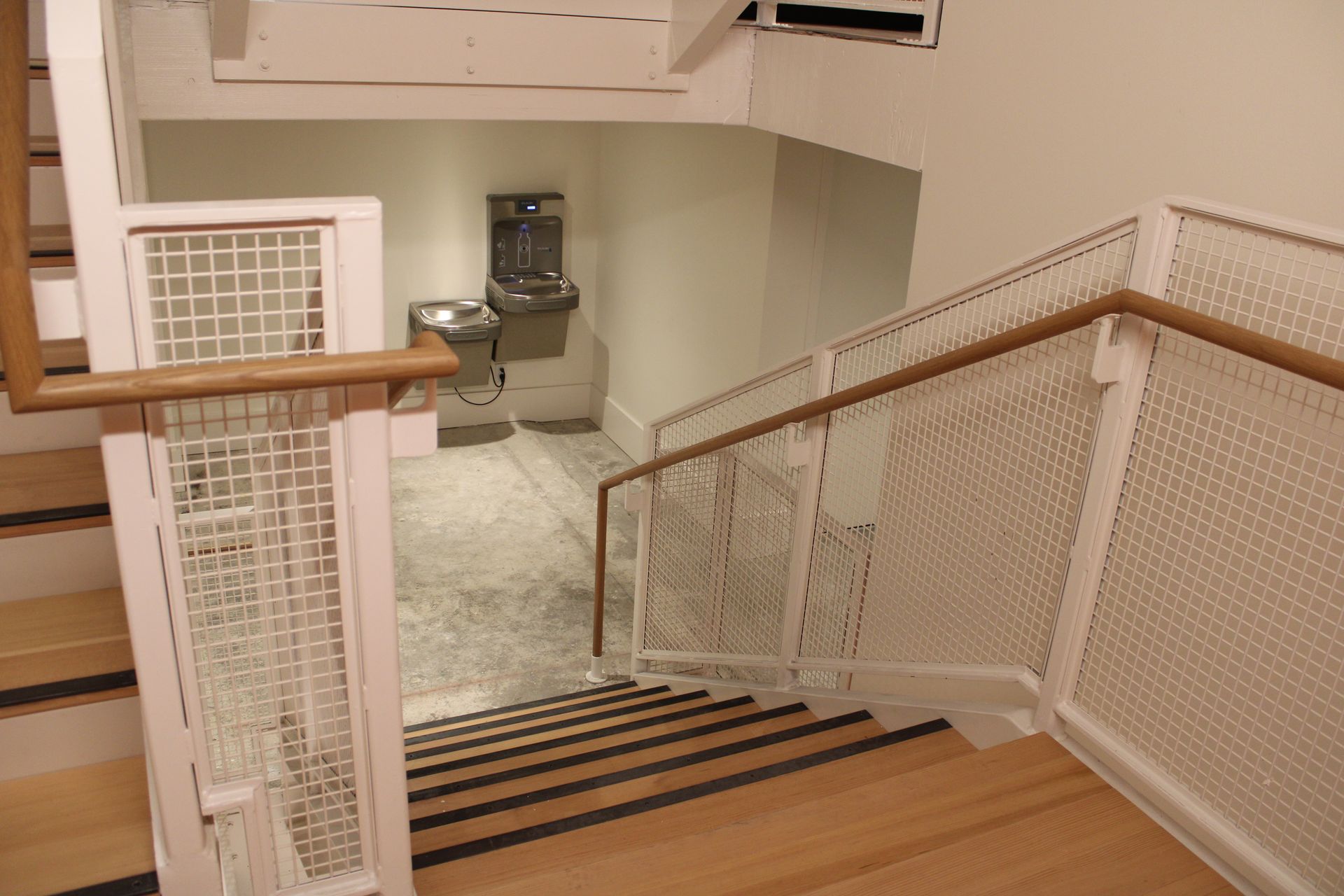 Staircase with light wood steps and white metal railings, leading down to a water fountain.