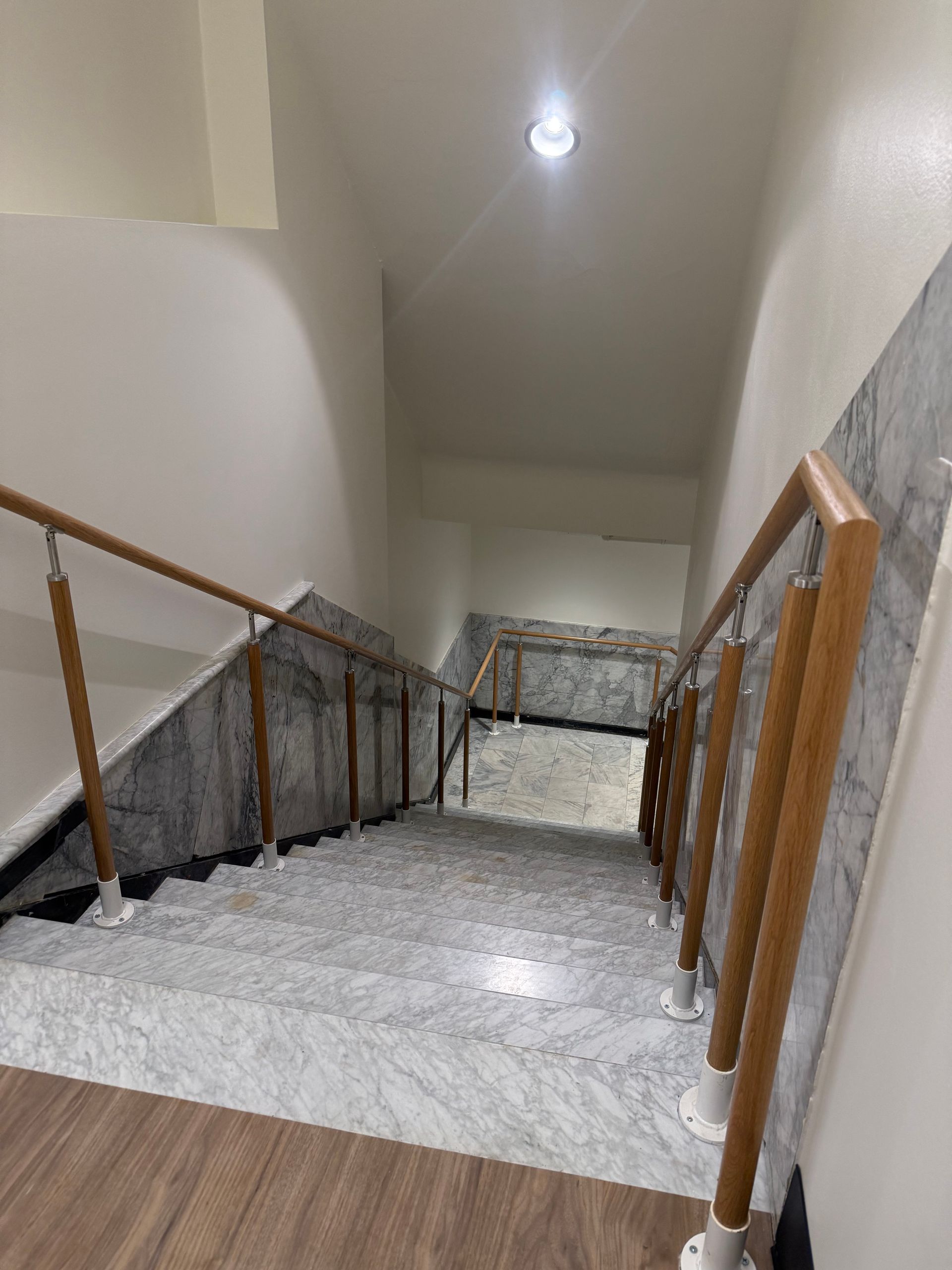 Staircase with marble steps, wooden handrails, and white walls. Descending view.