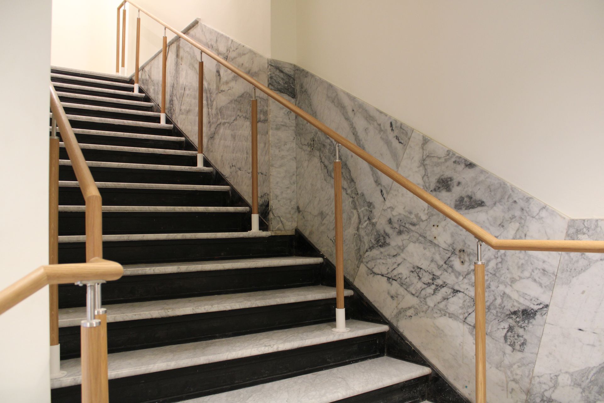 Staircase with wooden handrails. Black and white steps, marble wall.