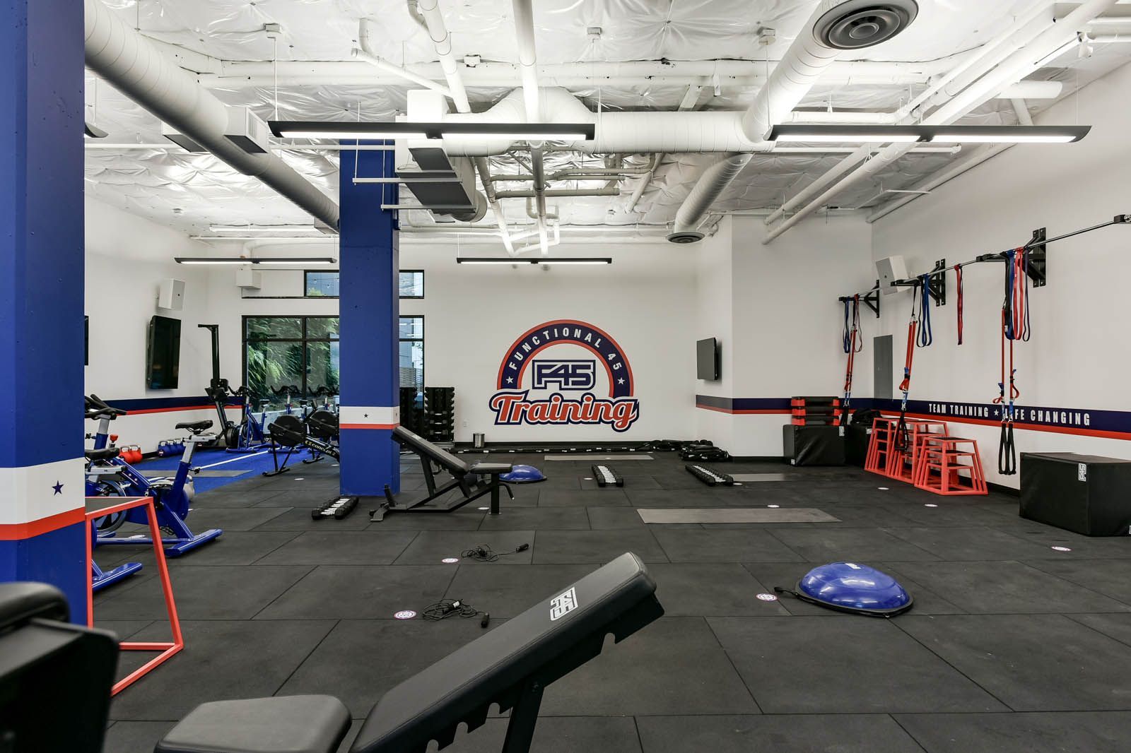 Gym interior with training equipment, including weights, mats, and benches; branded logo on the wall.