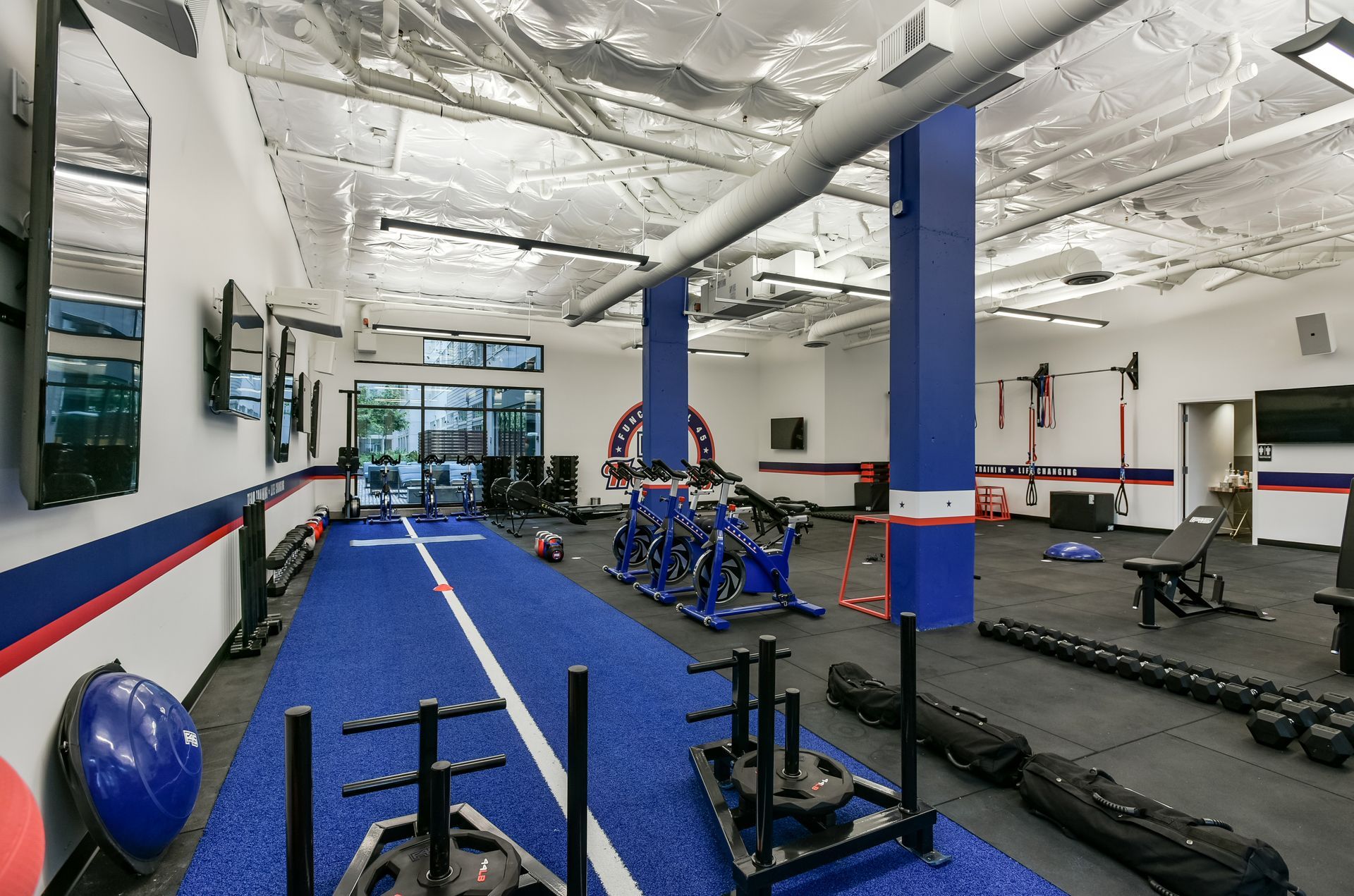 Interior of a gym with blue and red accents. Features workout equipment, including sleds and exercise machines.