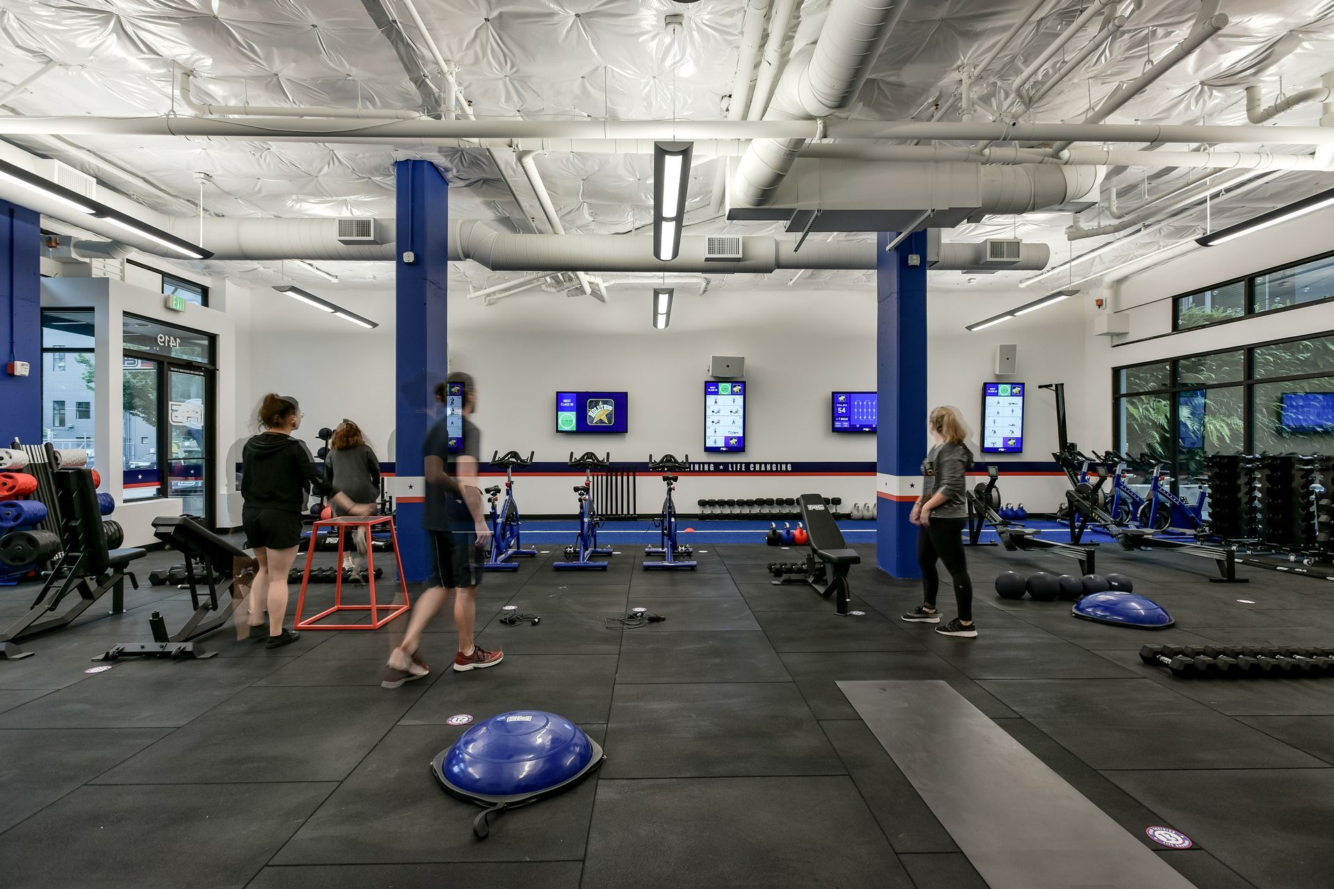 A gym interior with people working out, blue and white accents, exercise equipment.