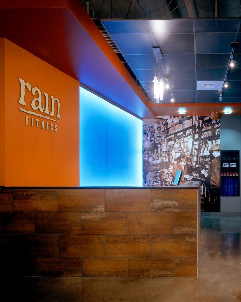Reception desk at Rain Fitness. Orange and wood paneling with blue backlit wall.