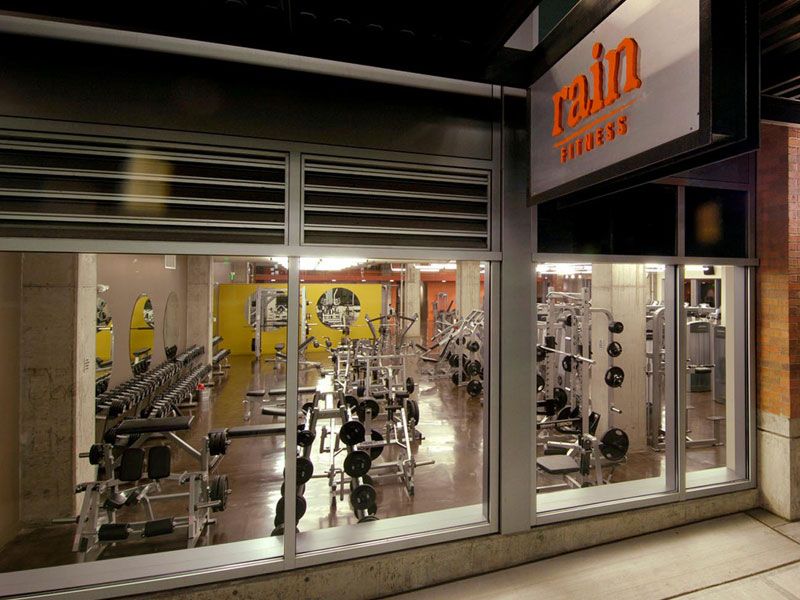 Exterior of Rain Fitness gym; weightlifting equipment visible through large windows.