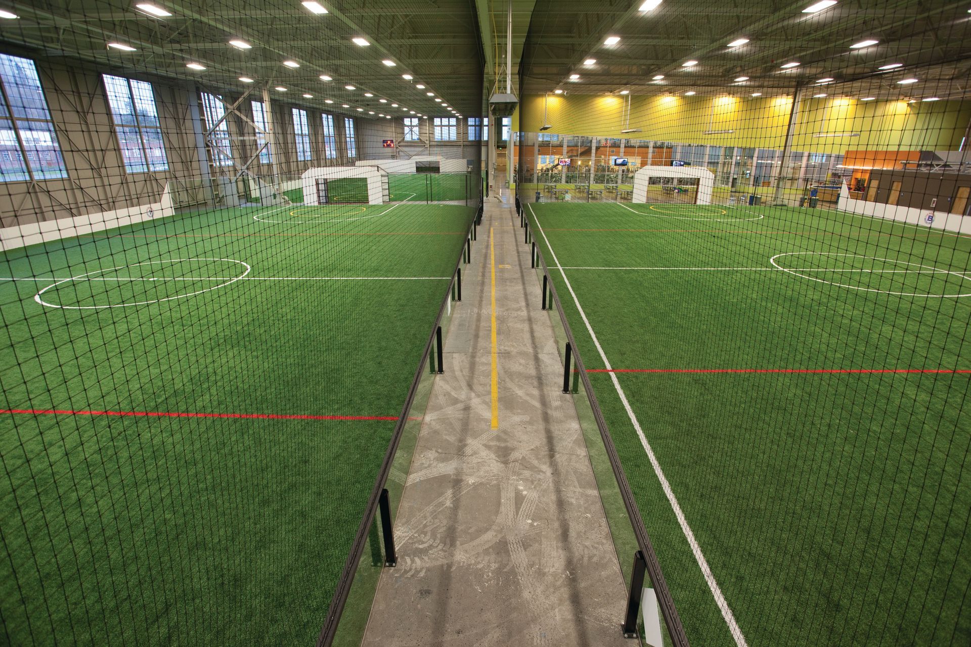 Indoor soccer field with artificial turf, nets, goals, and a central walkway.