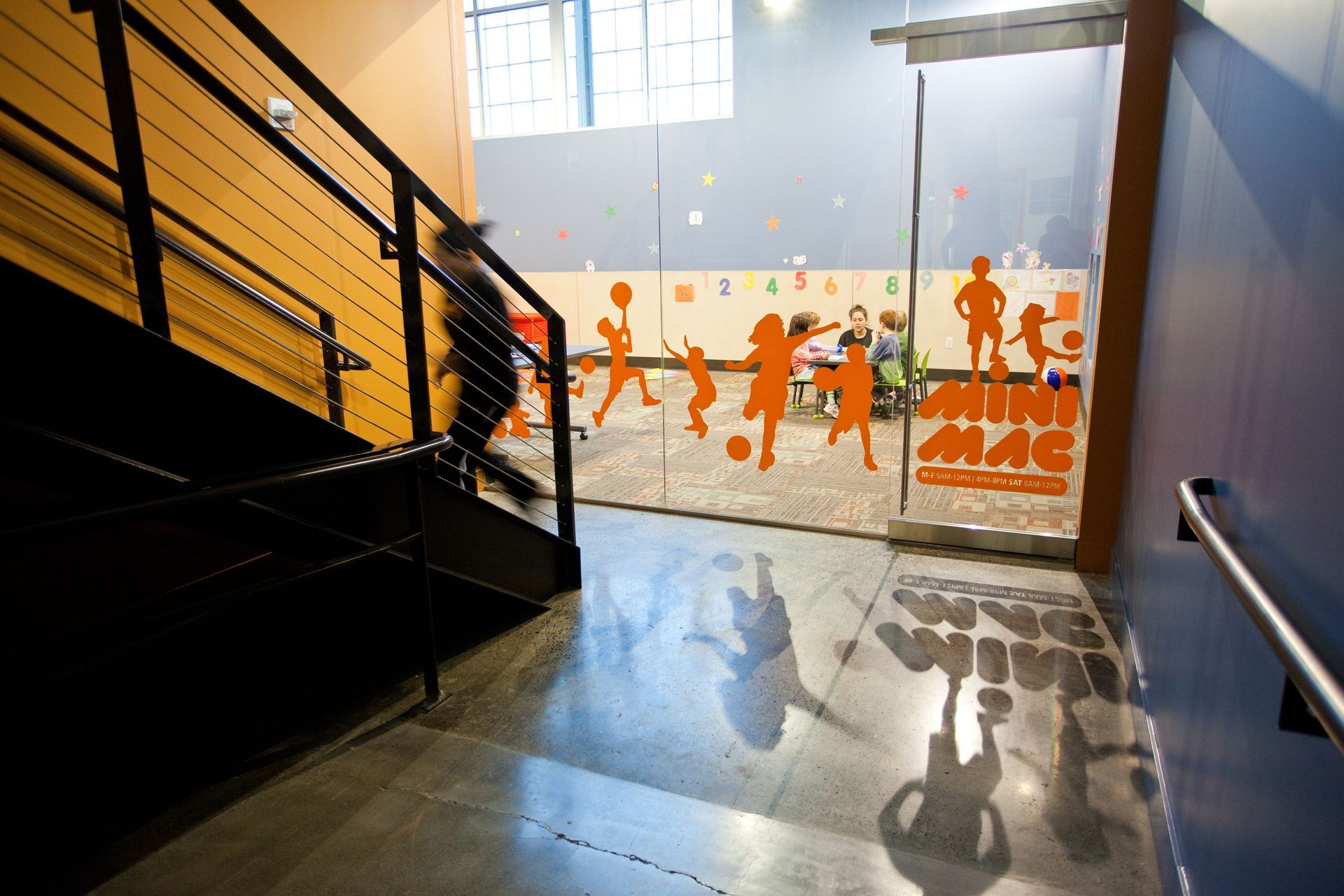 Staircase leading to a glass door with orange silhouettes of children playing inside a brightly lit room.