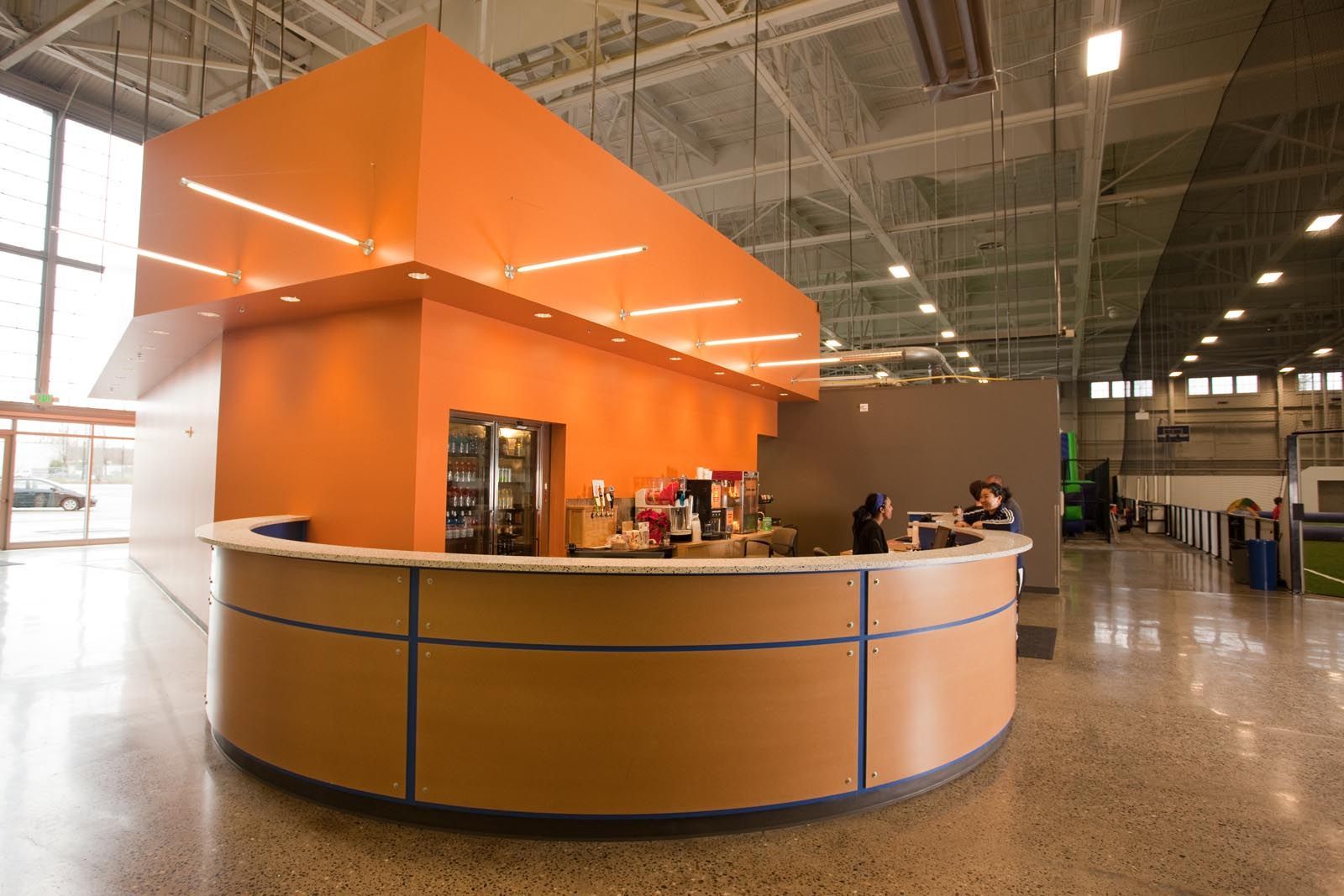 Orange and tan reception desk in a brightly lit indoor sports facility.