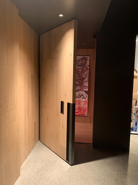 Large wooden pivot door, partially open, with dark metal handle. Interior with art.