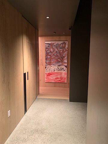 Narrow hallway with light wood cabinets, gray carpet, and a colorful abstract painting.