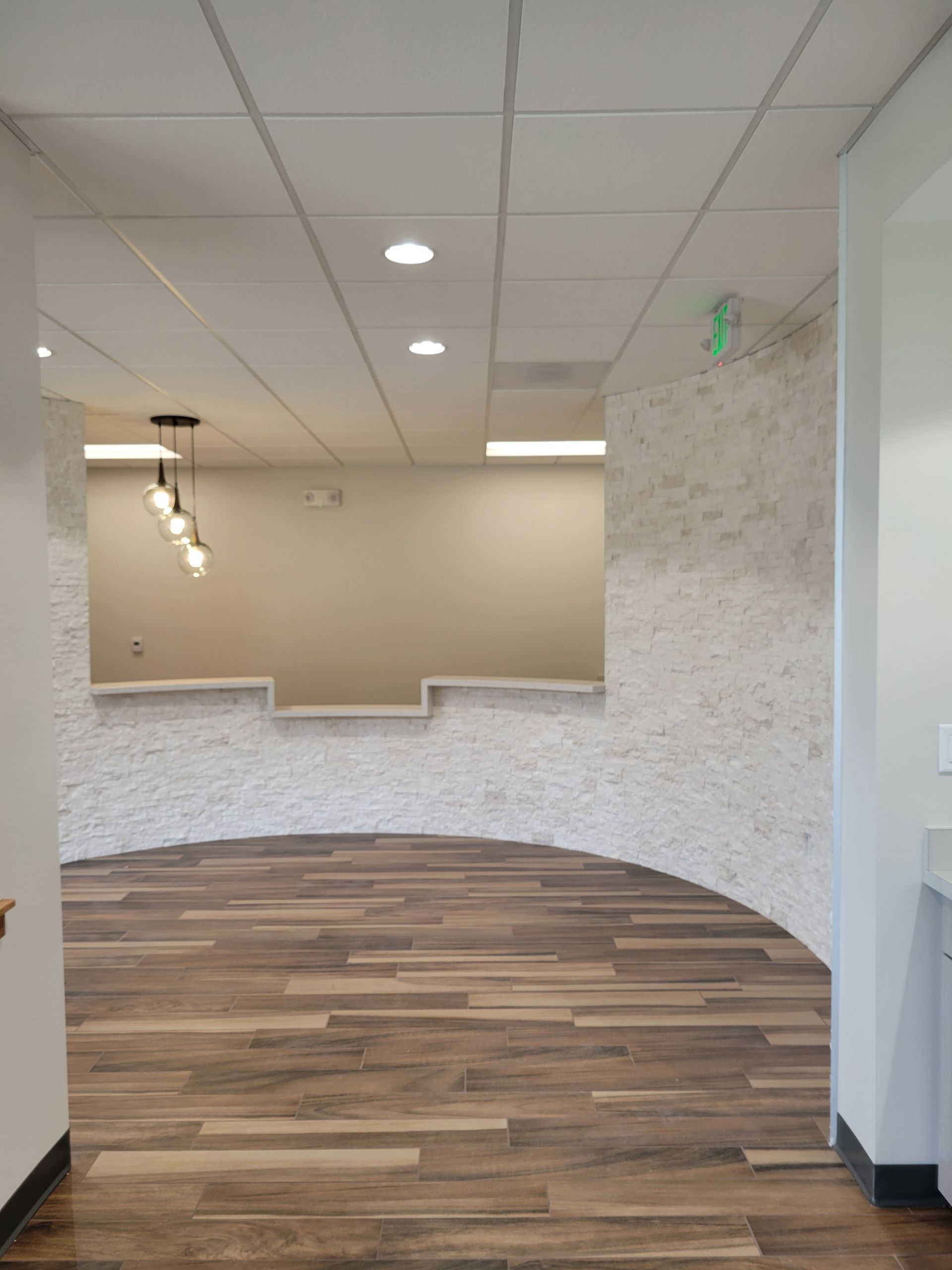 Reception area with wood floor, white textured wall, and overhead lighting.