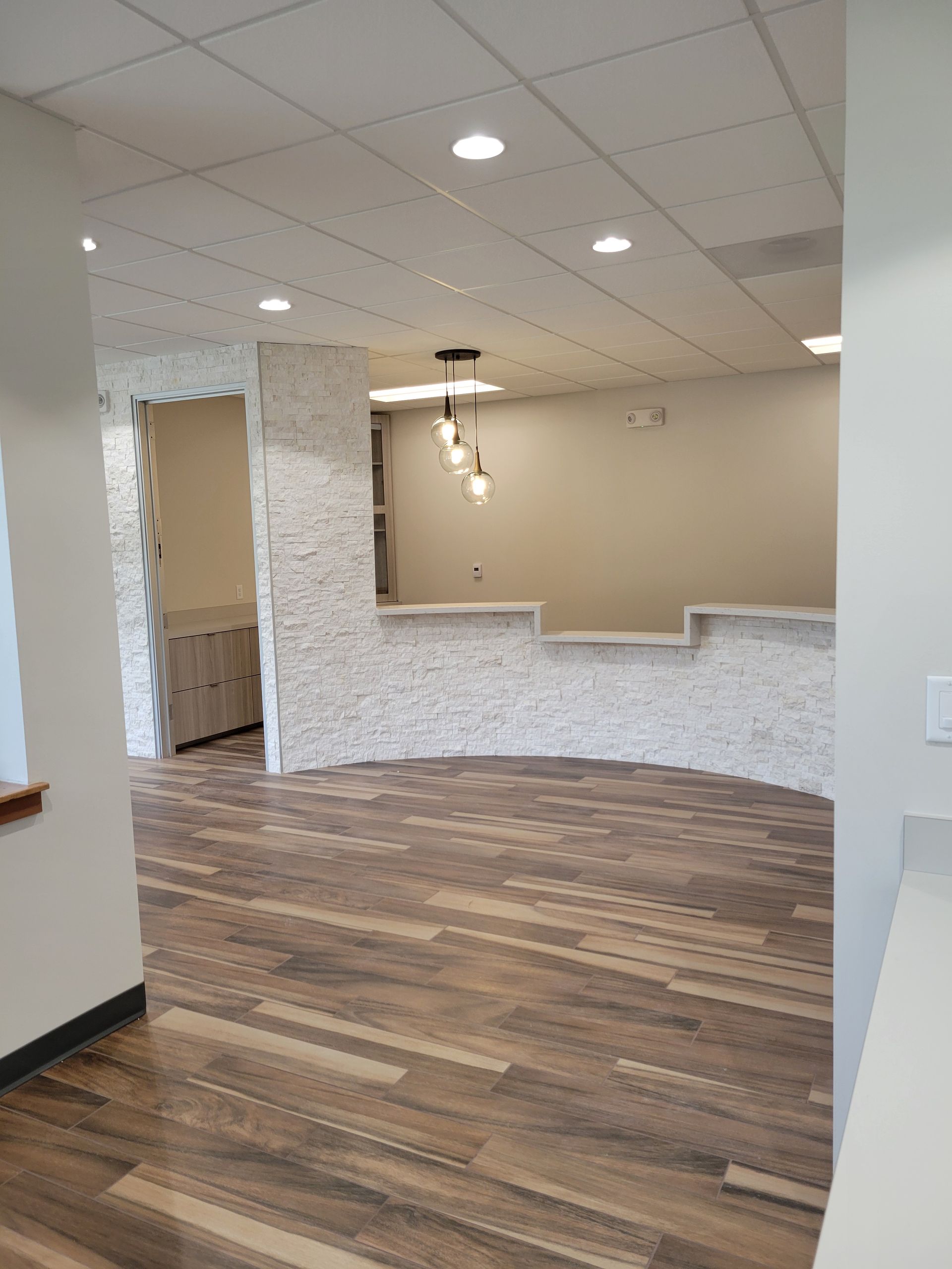 Empty reception area with wood flooring, stone accent wall, and recessed lighting.