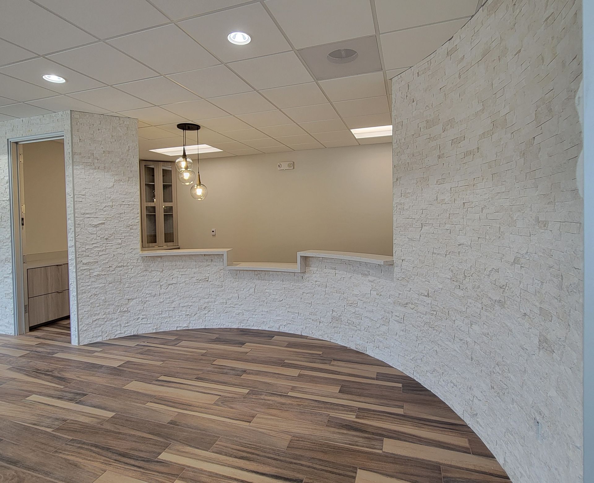 Modern office interior with curved textured wall and arched opening, revealing another room.
