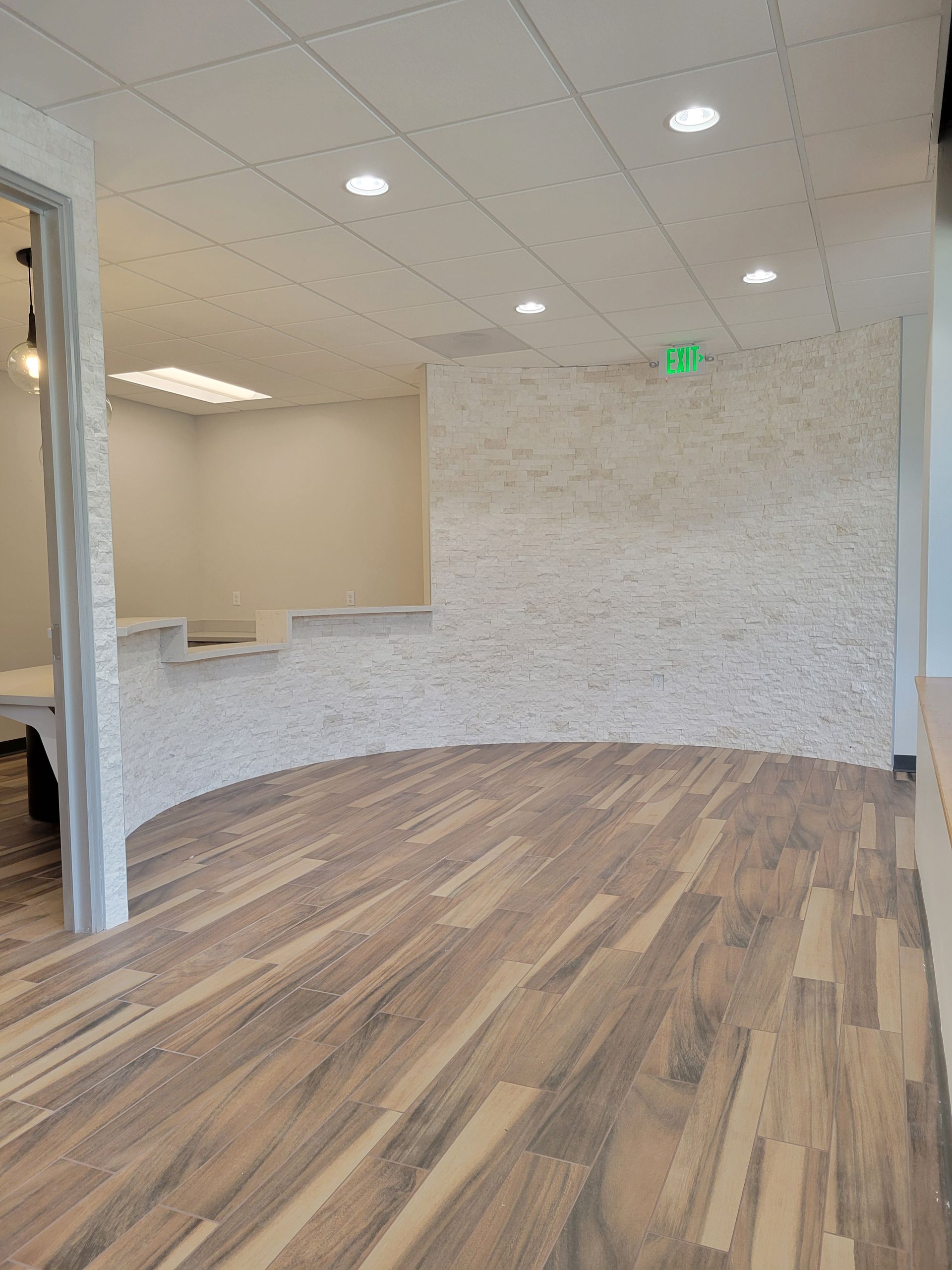 Interior view of a modern reception area with wood floors, textured white wall, and recessed lighting.