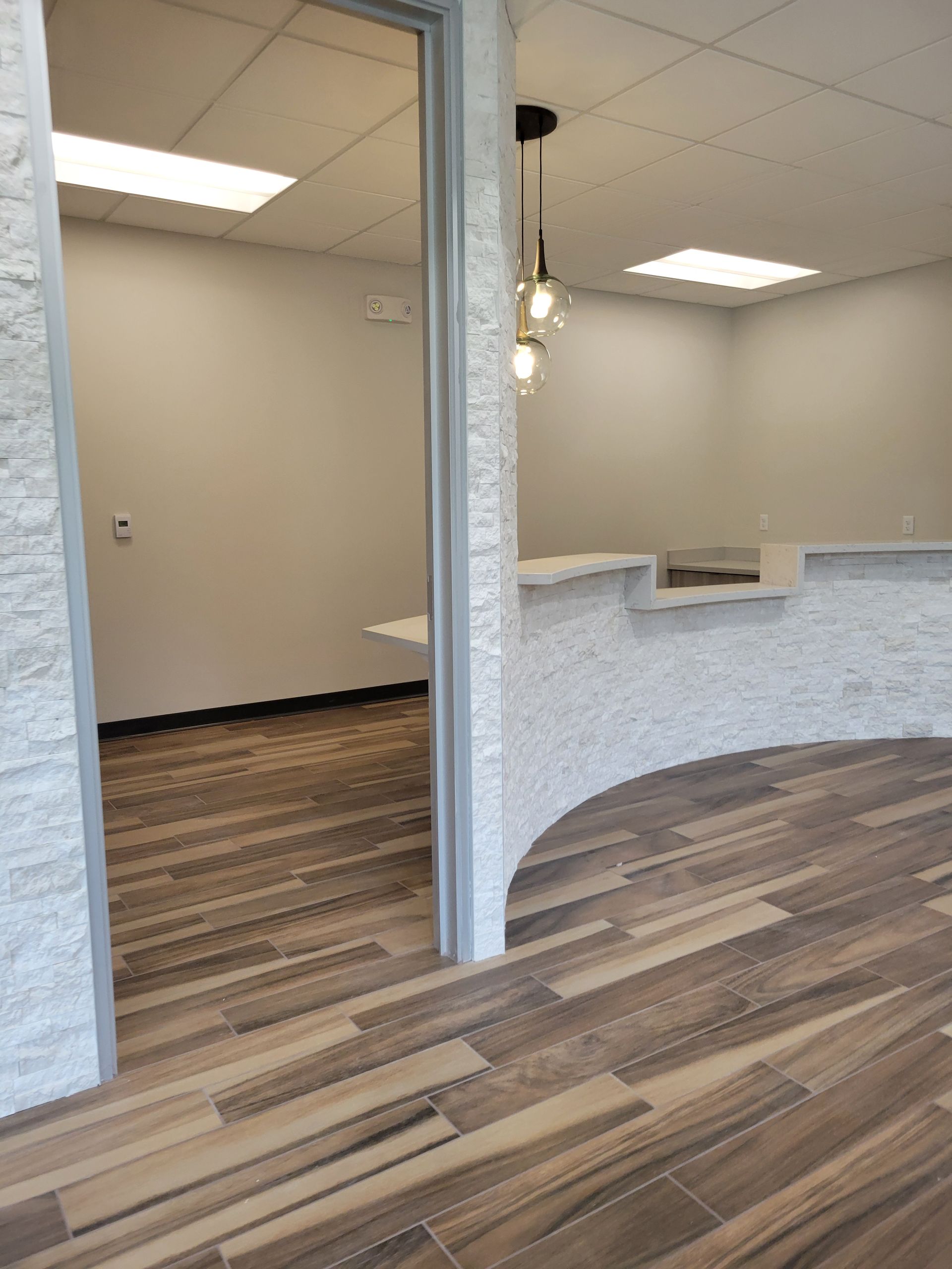 Interior with textured white wall, wooden floor, and a reception desk with three hanging lights.