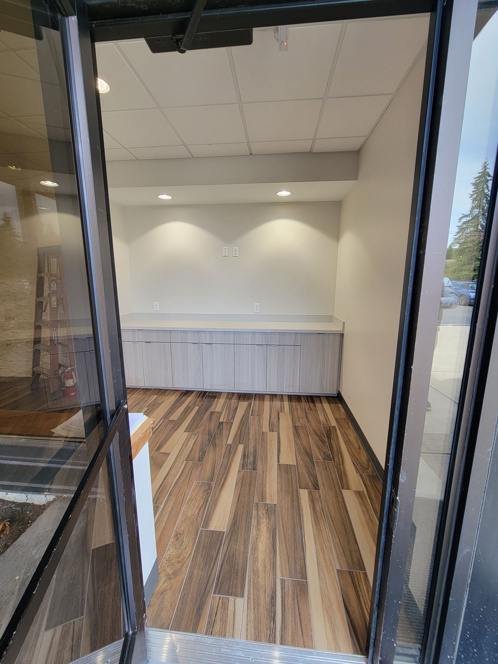 View from doorway into a room with wood floors, cabinets, and a white wall with recessed lights.