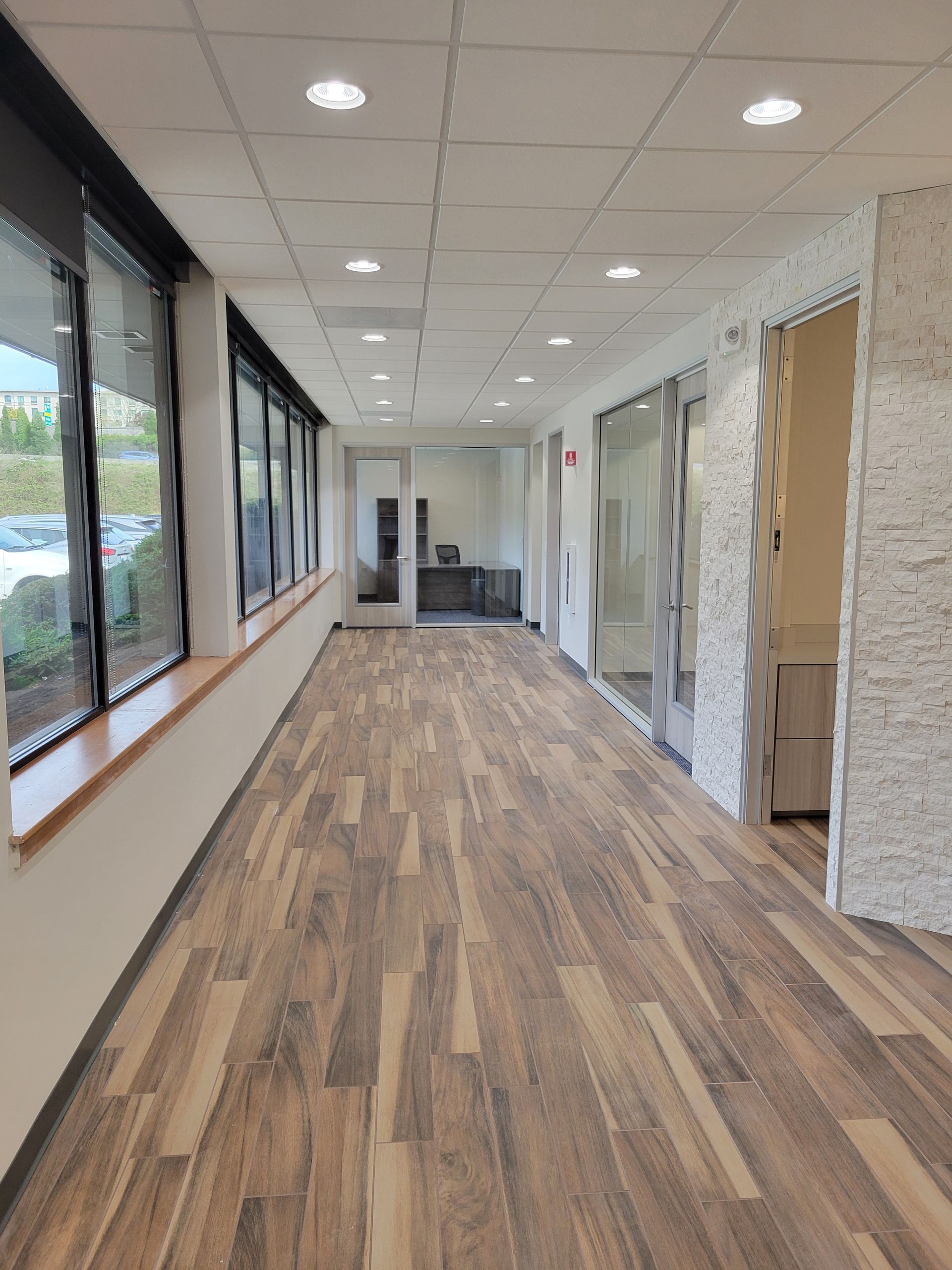 Long hallway with wood-look flooring, large windows, recessed lights, and doors on the right.
