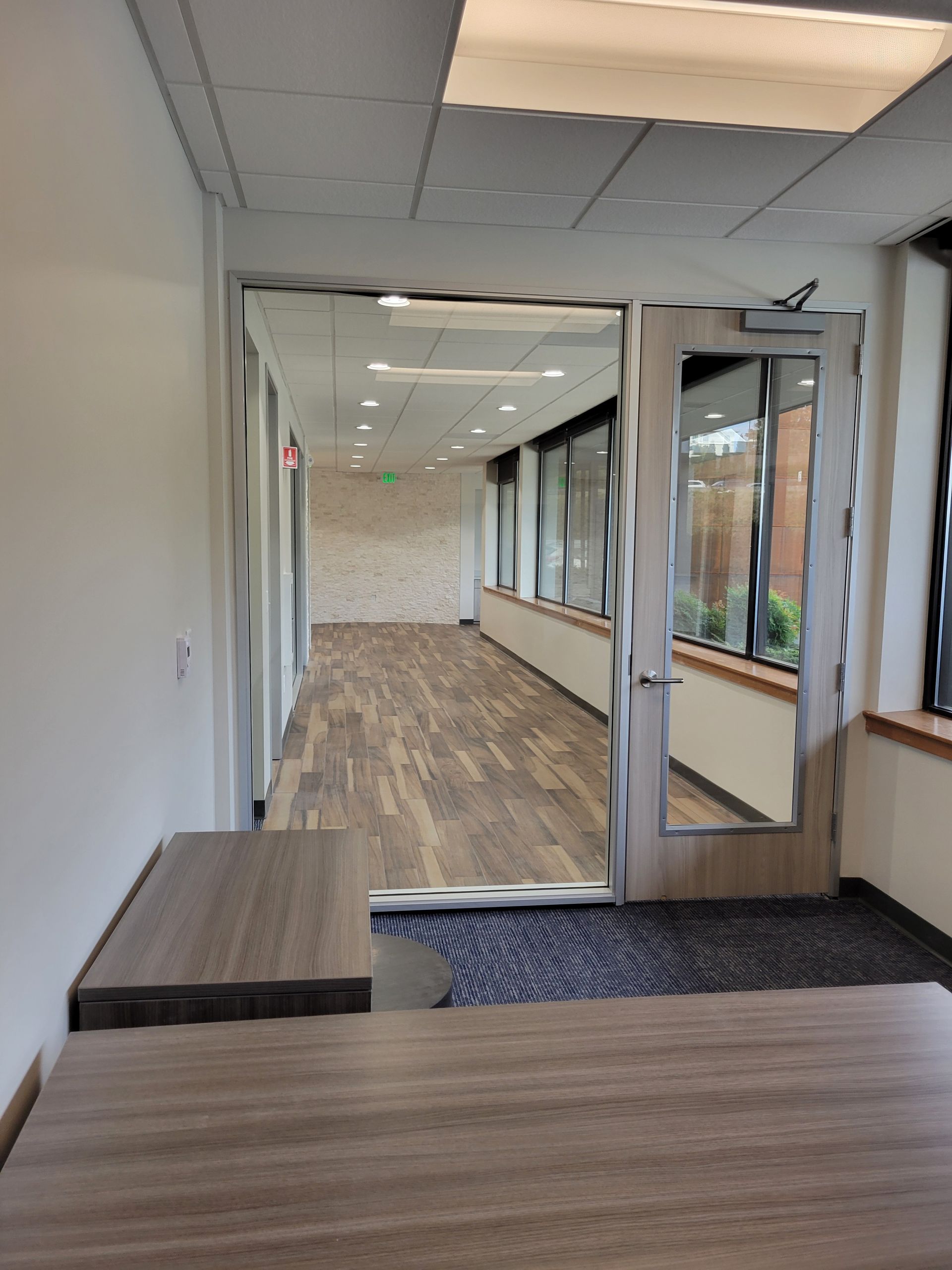 Hallway with wood flooring, door with windows, and a long row of windows along the wall.