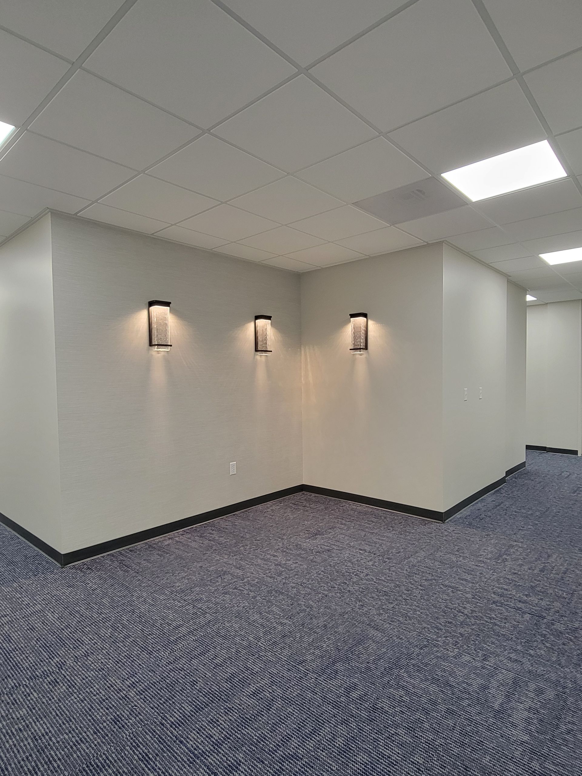 Empty hallway with blue patterned carpet, white walls, and three wall sconces.