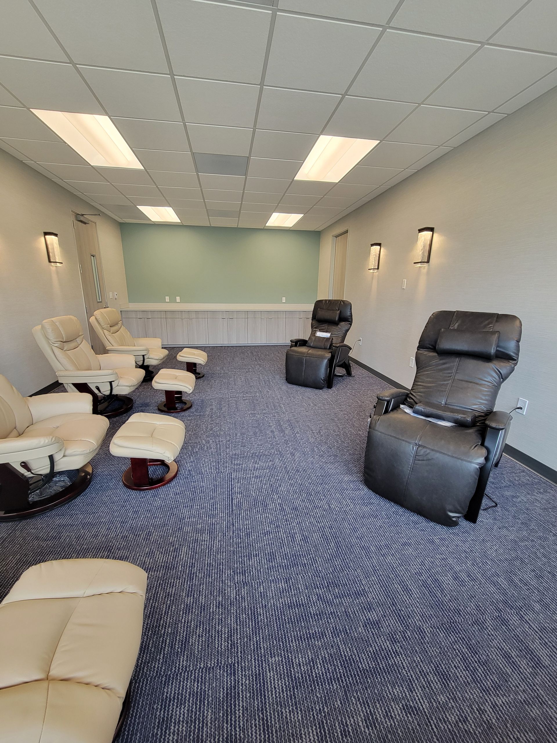 Room with massage chairs and footrests, patterned carpet, and recessed lighting.