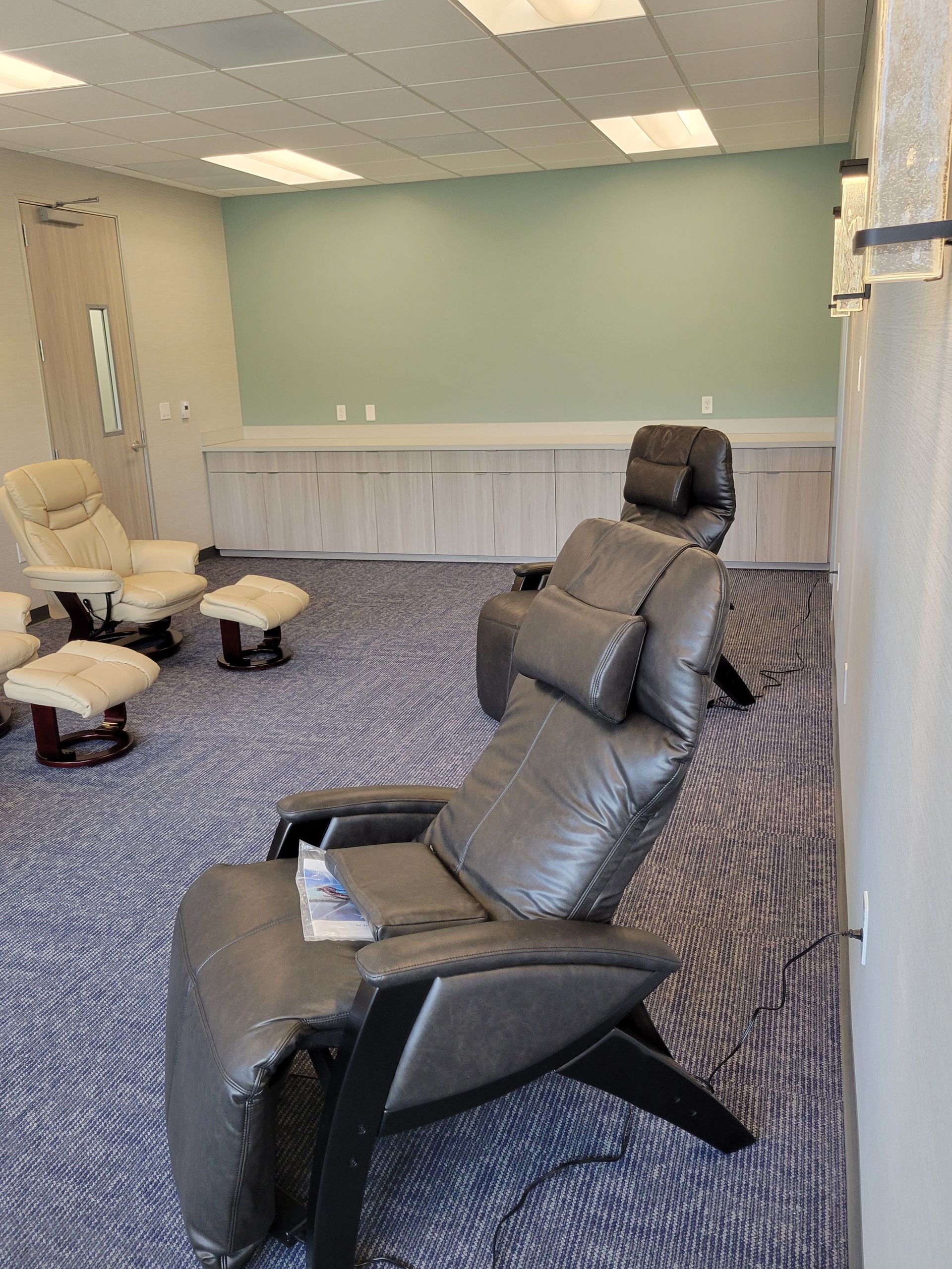 Relaxation room with reclining chairs, footstools, and blue patterned carpet. Light green wall and cabinets along the back.
