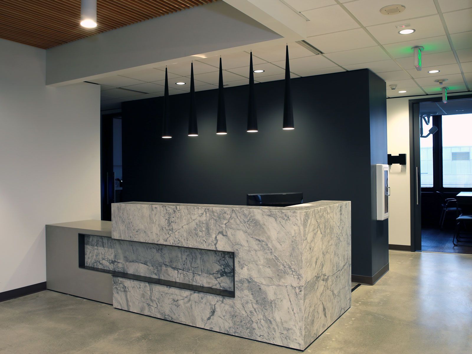Modern office reception area with granite front desk and dark wall, pendant lights, and door.