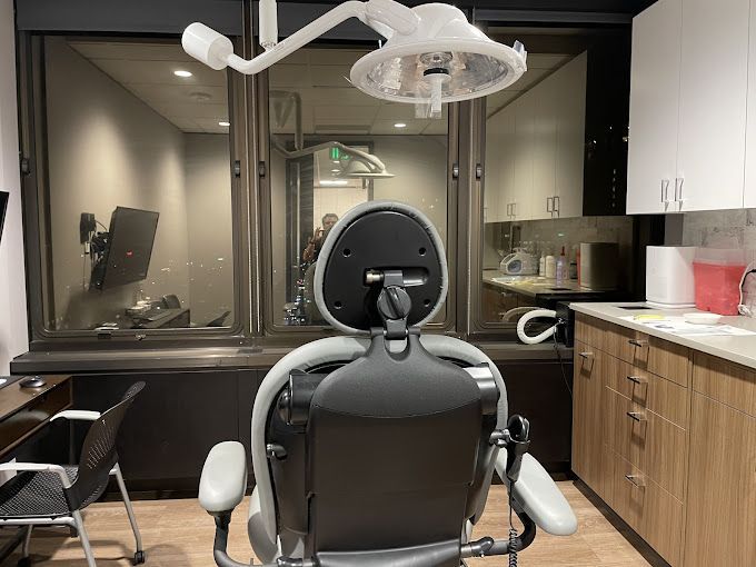 Dental chair in a dentist's office with window view, cabinet, and overhead light.