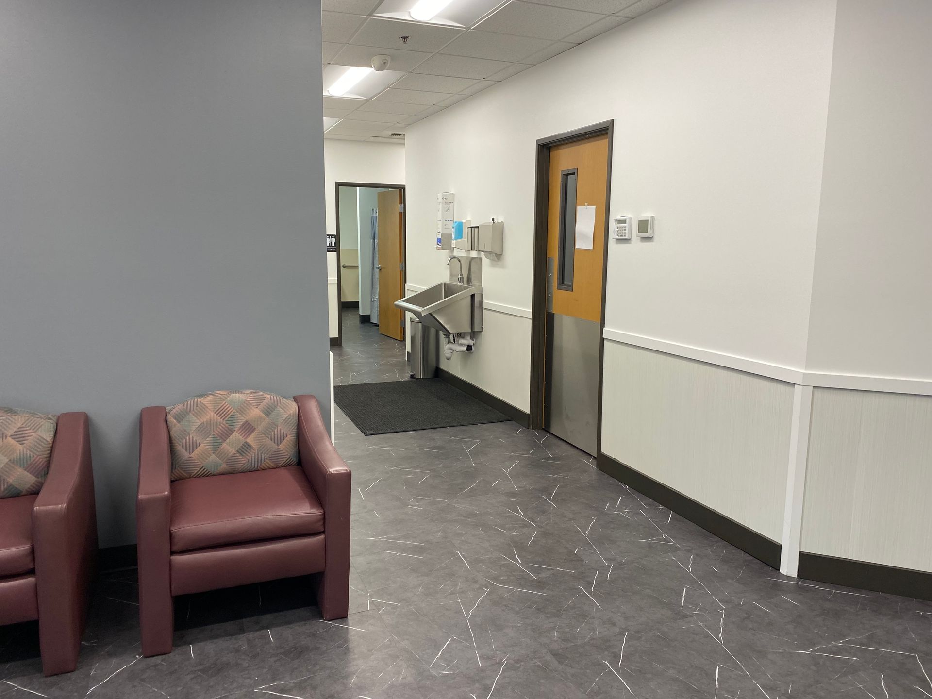 Medical office hallway with seating, sink, and doors. Walls are gray and white.