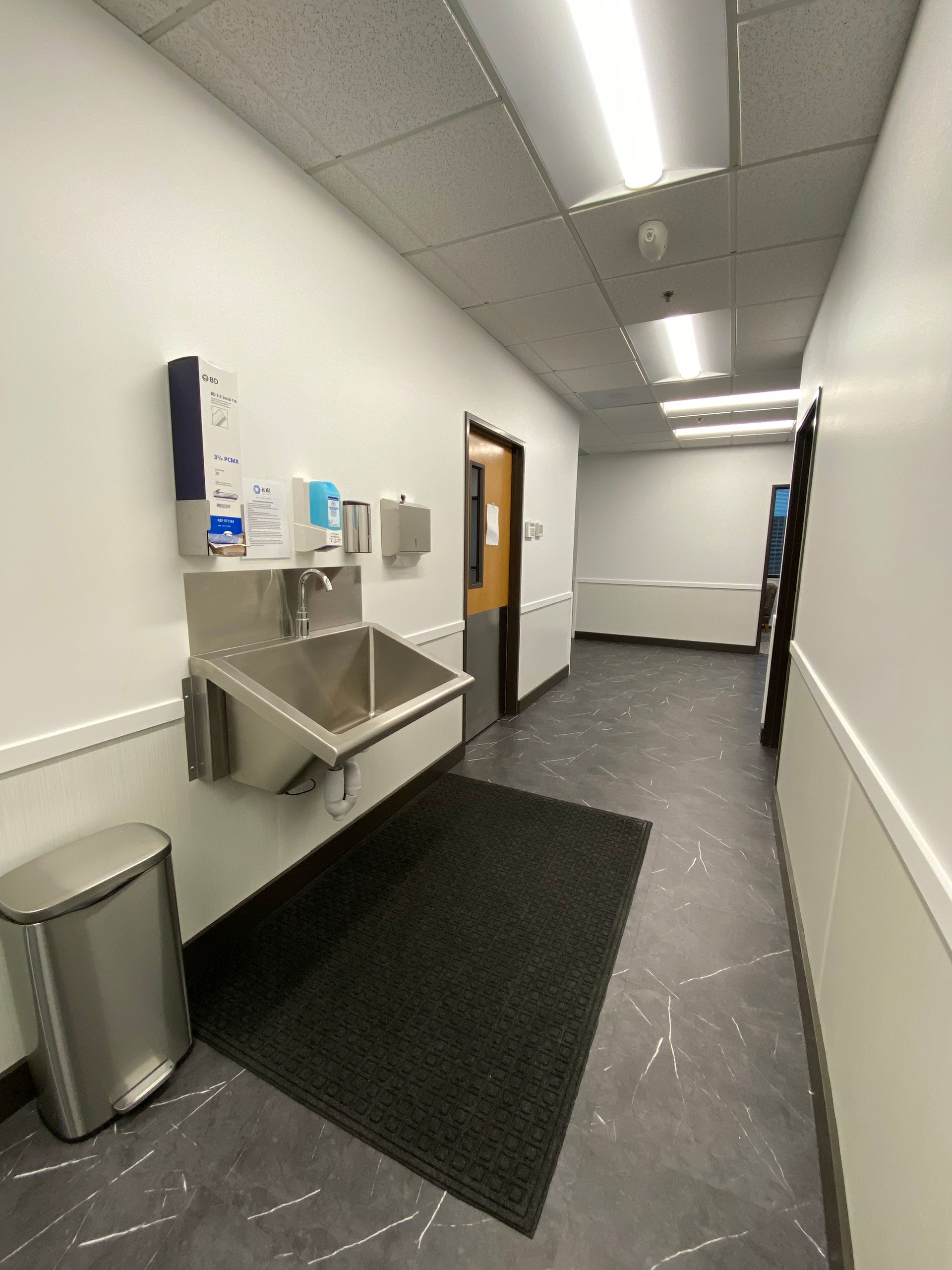Hallway with stainless steel sink, trash can, and hand sanitizer dispenser.