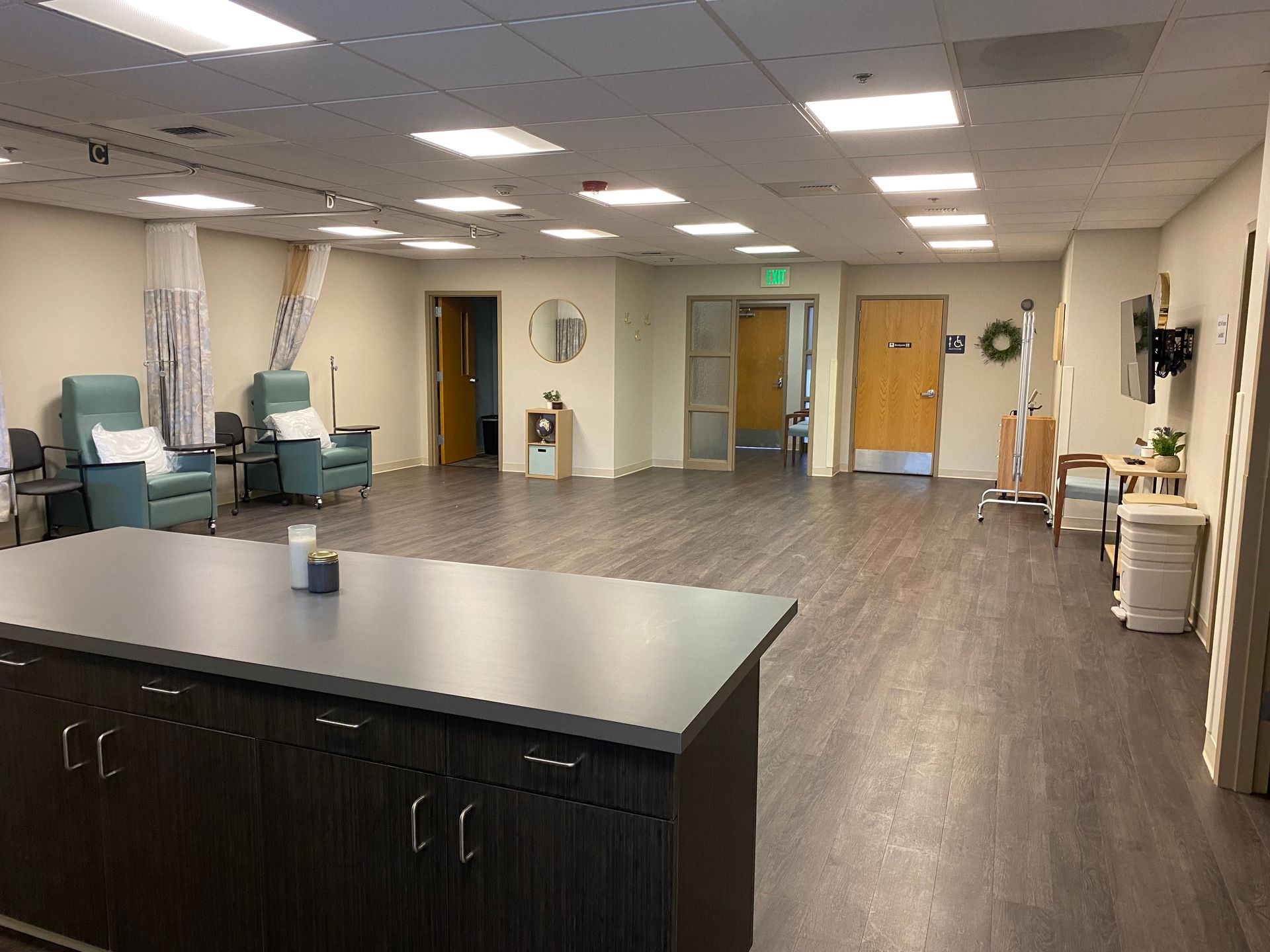 A large, open room with dark wood flooring, chairs, and multiple doorways. A dark countertop is in the foreground.