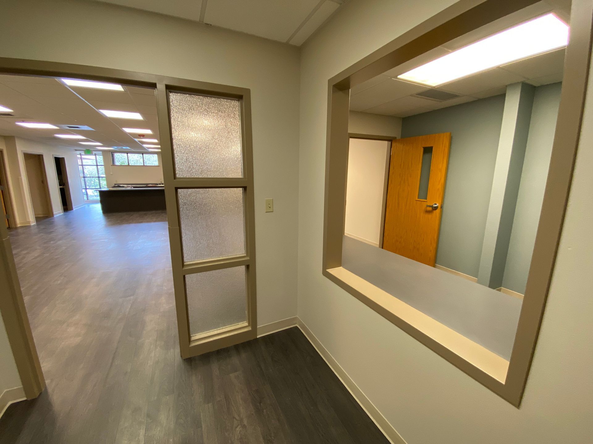 Interior hallway with doorways and windows, showing office space with wood-look flooring and light-colored walls.