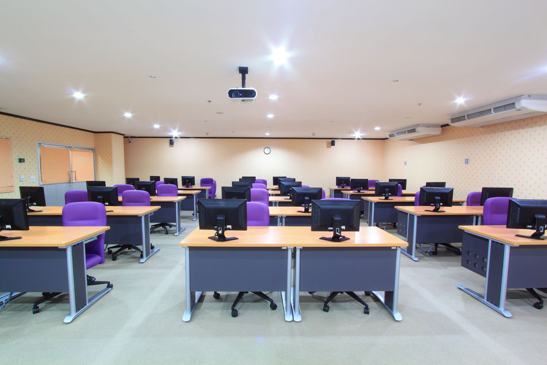 Computer lab: rows of desks with computers and purple chairs; projector on ceiling.