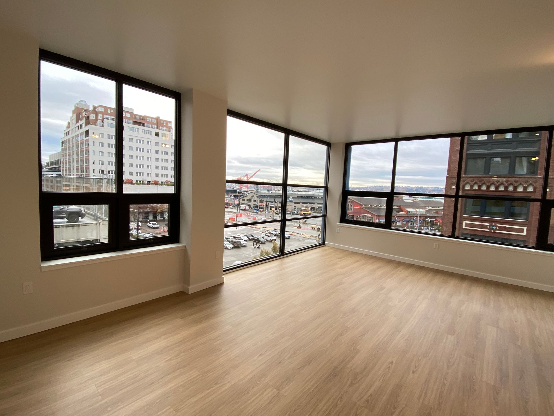Empty modern room with large windows overlooking city buildings and parking area.