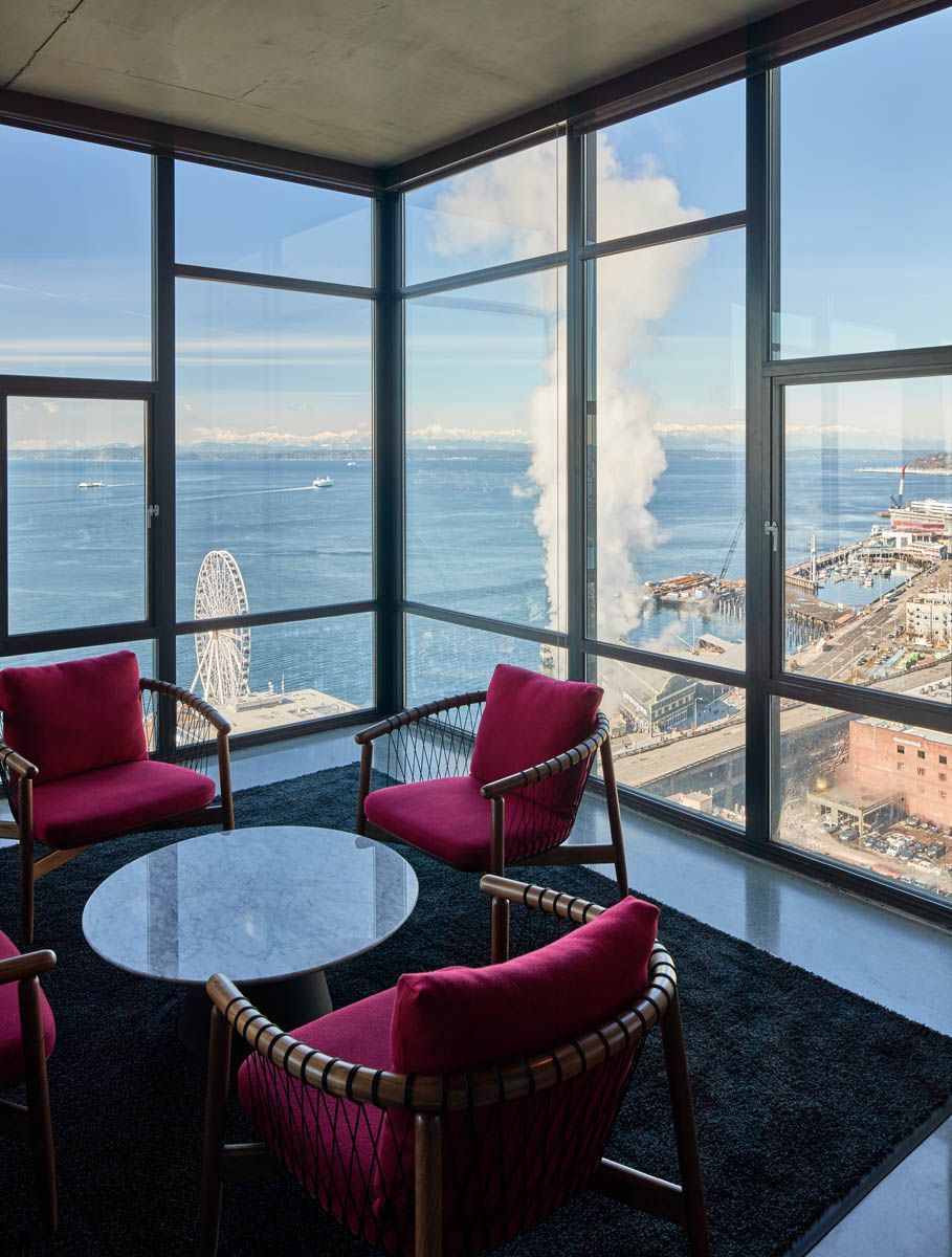 Room with waterfront view; red chairs around a table on a dark rug.