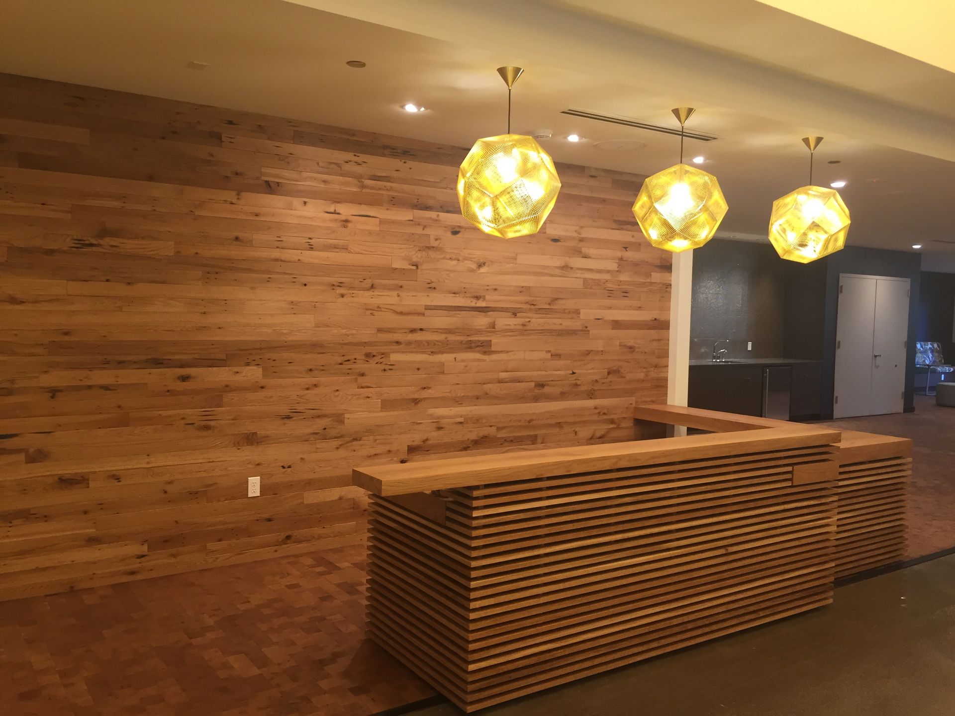 Wooden reception desk and wall with three globe-shaped pendant lights hanging above.