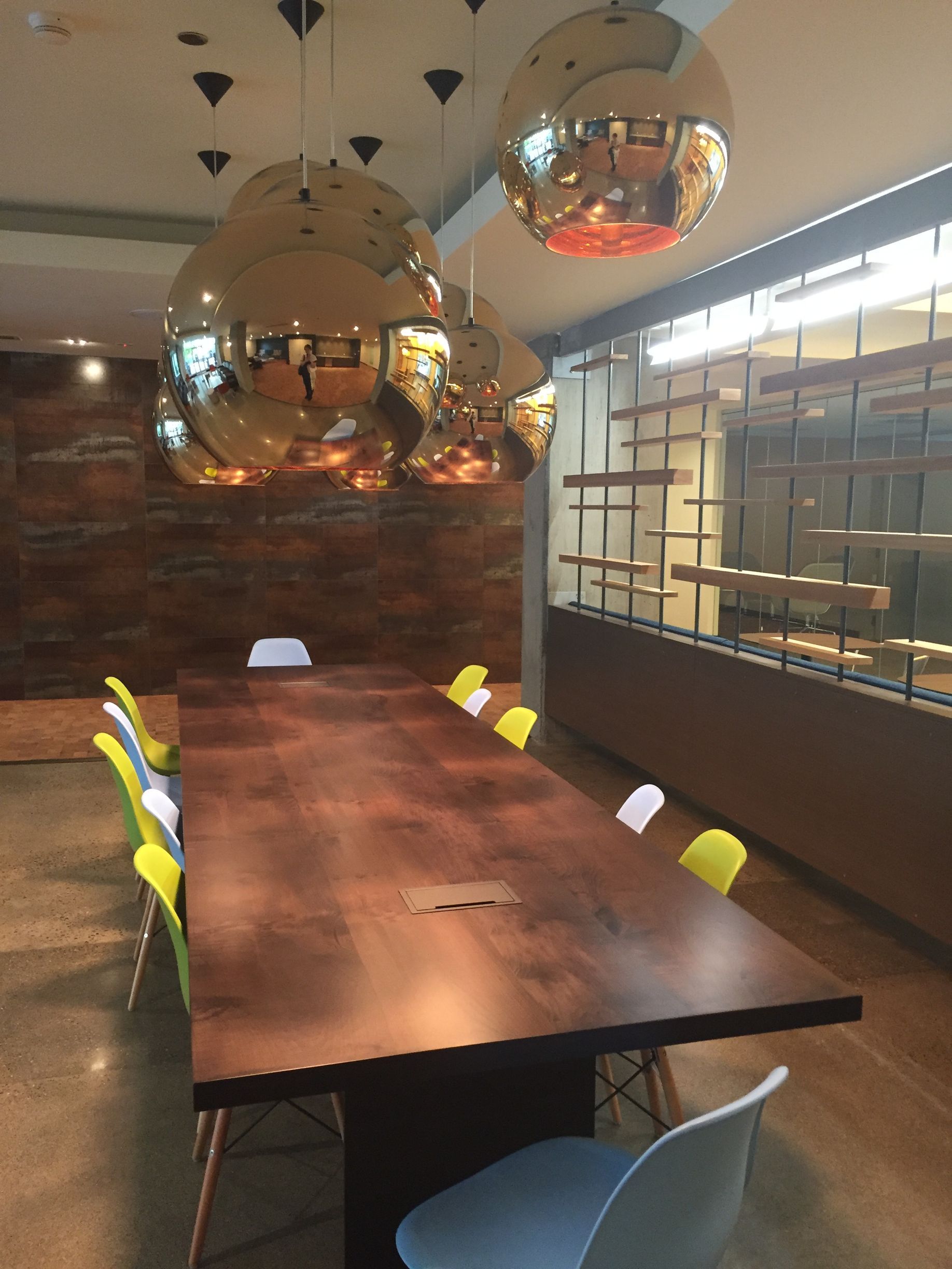 Meeting room with large wood table, colorful chairs, and gold orb pendant lights.