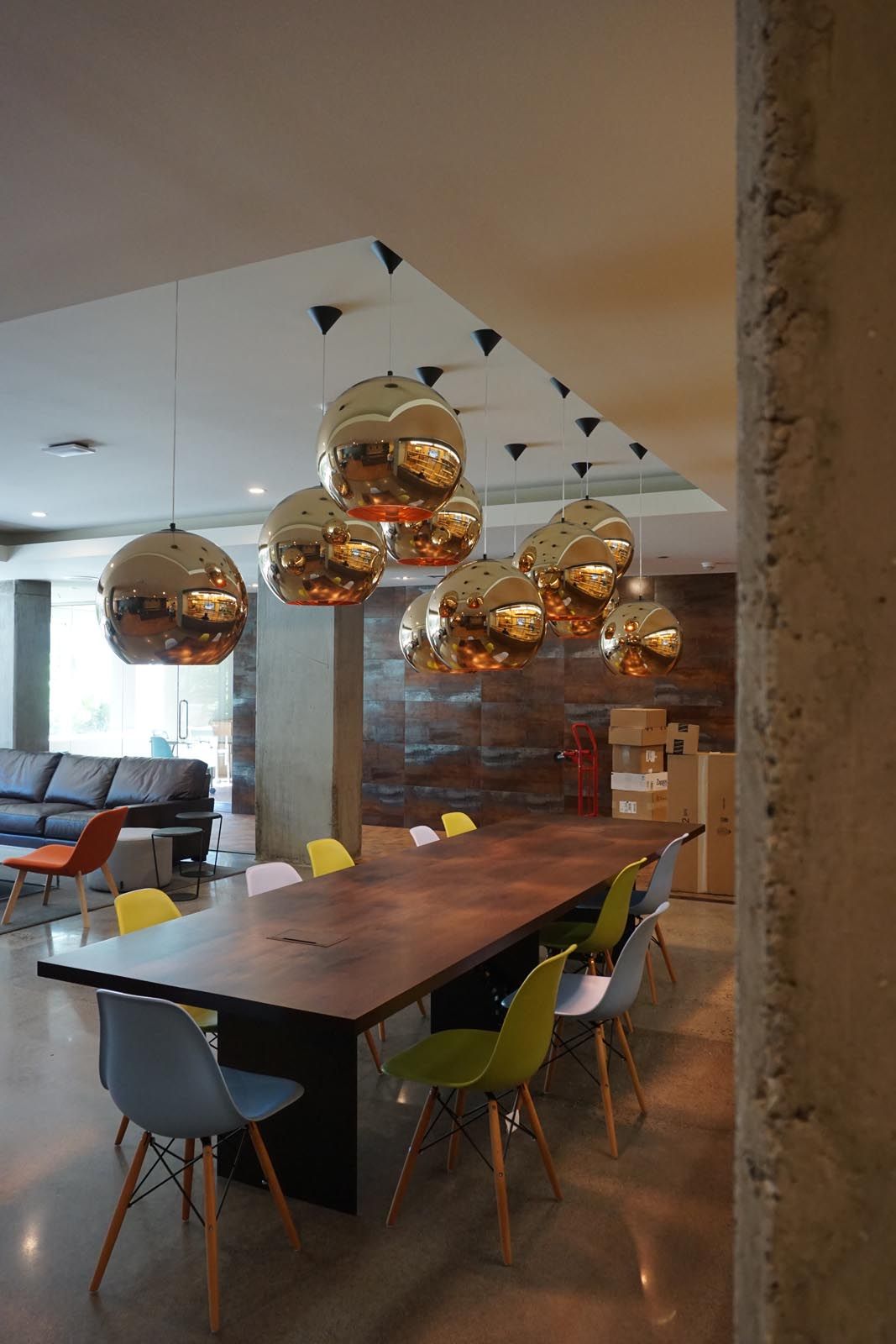 A long wooden table with colorful chairs, metallic globe lights hanging above.