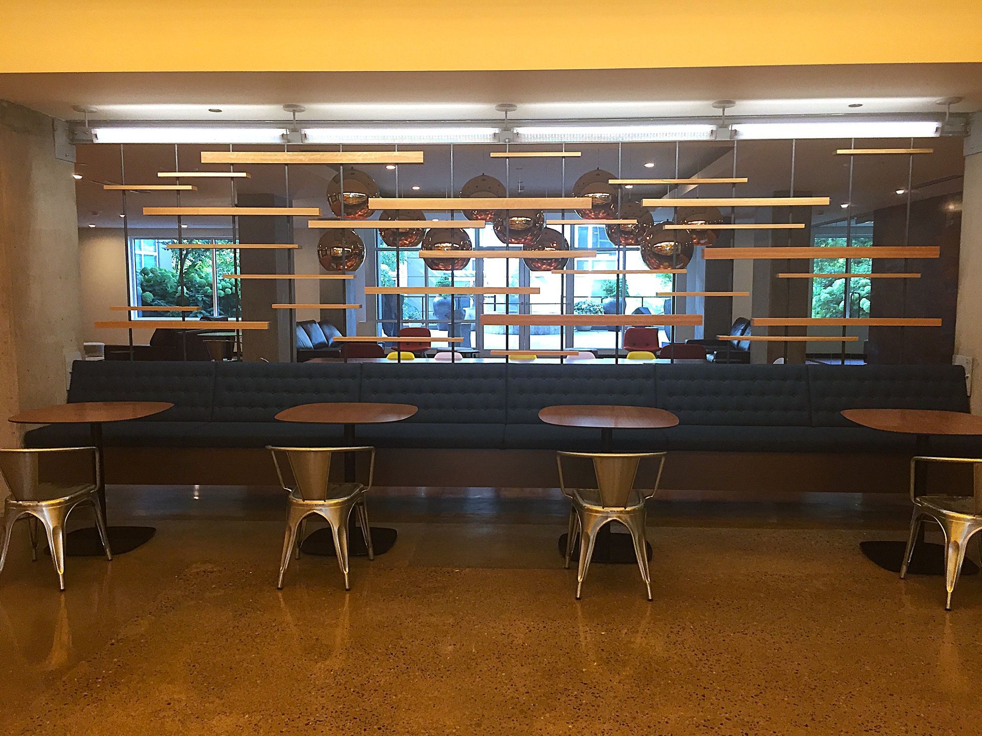 A long blue bench with small tables and silver chairs, against a wall with floating wooden shelves.