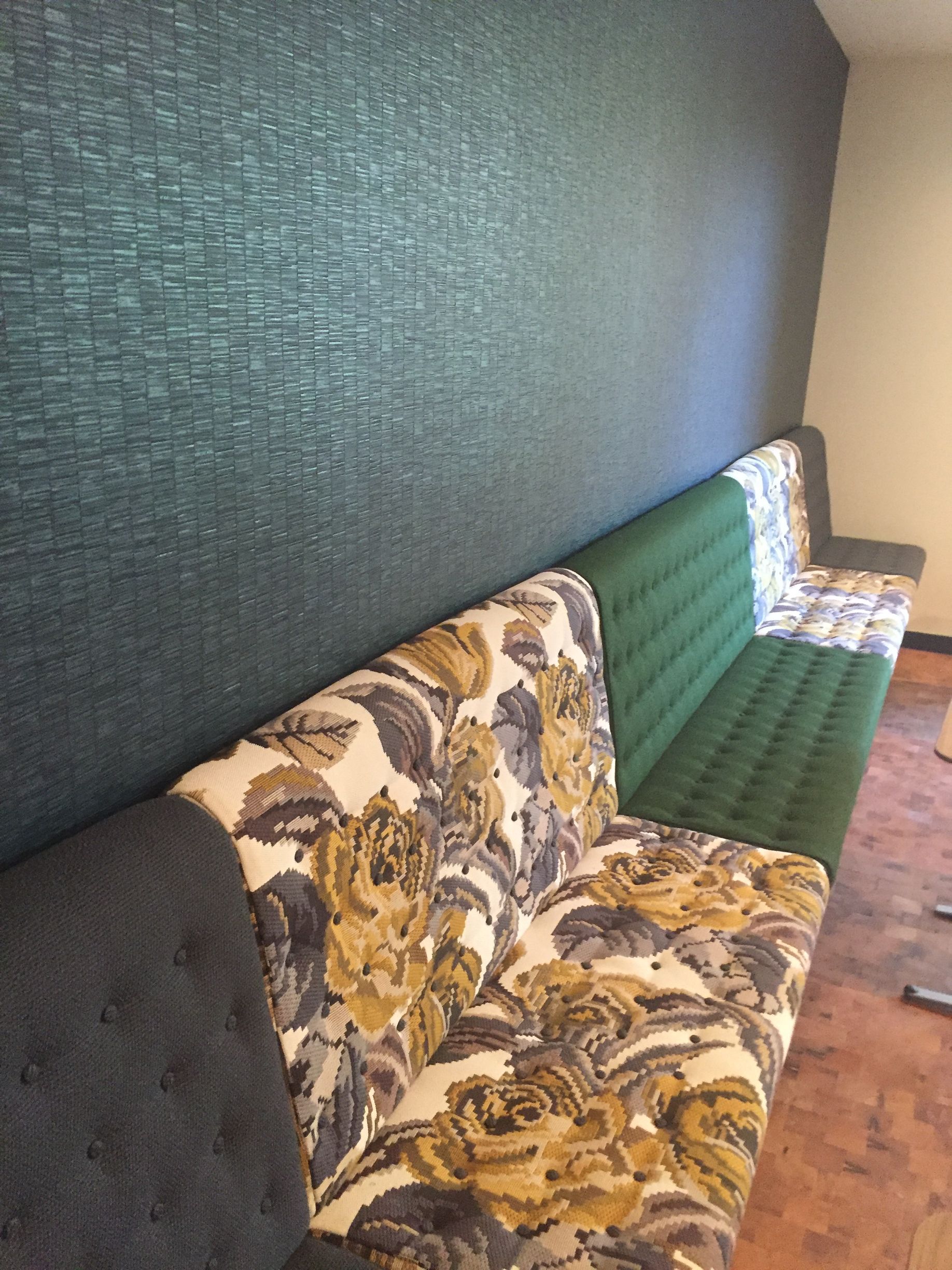 Long green and floral patterned sofa against a textured teal wall.