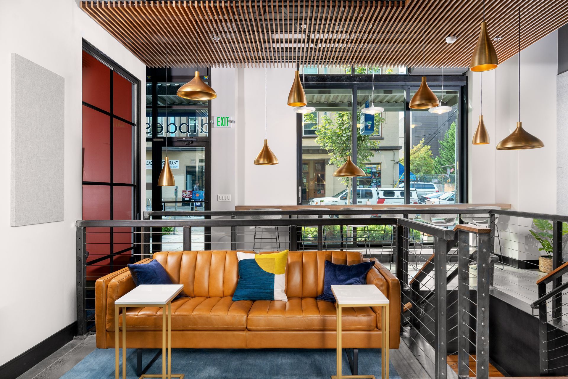Lounge area with brown leather couch, gold pendant lights, and large windows.