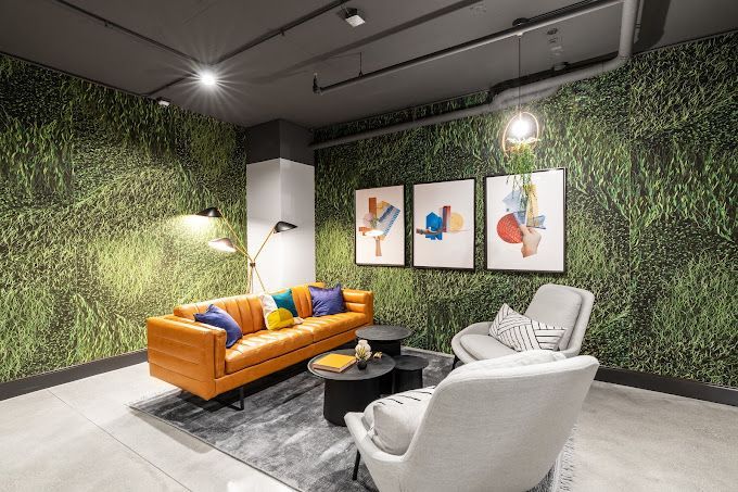 Living room with orange leather sofa, two armchairs, artwork, and grass-print wallpaper.