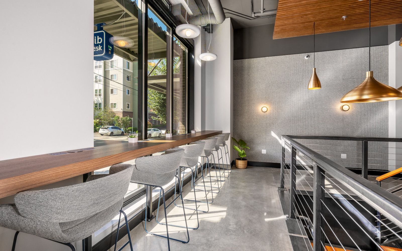Cafe interior with window seating, gray chairs, wooden counter, and hanging lights.