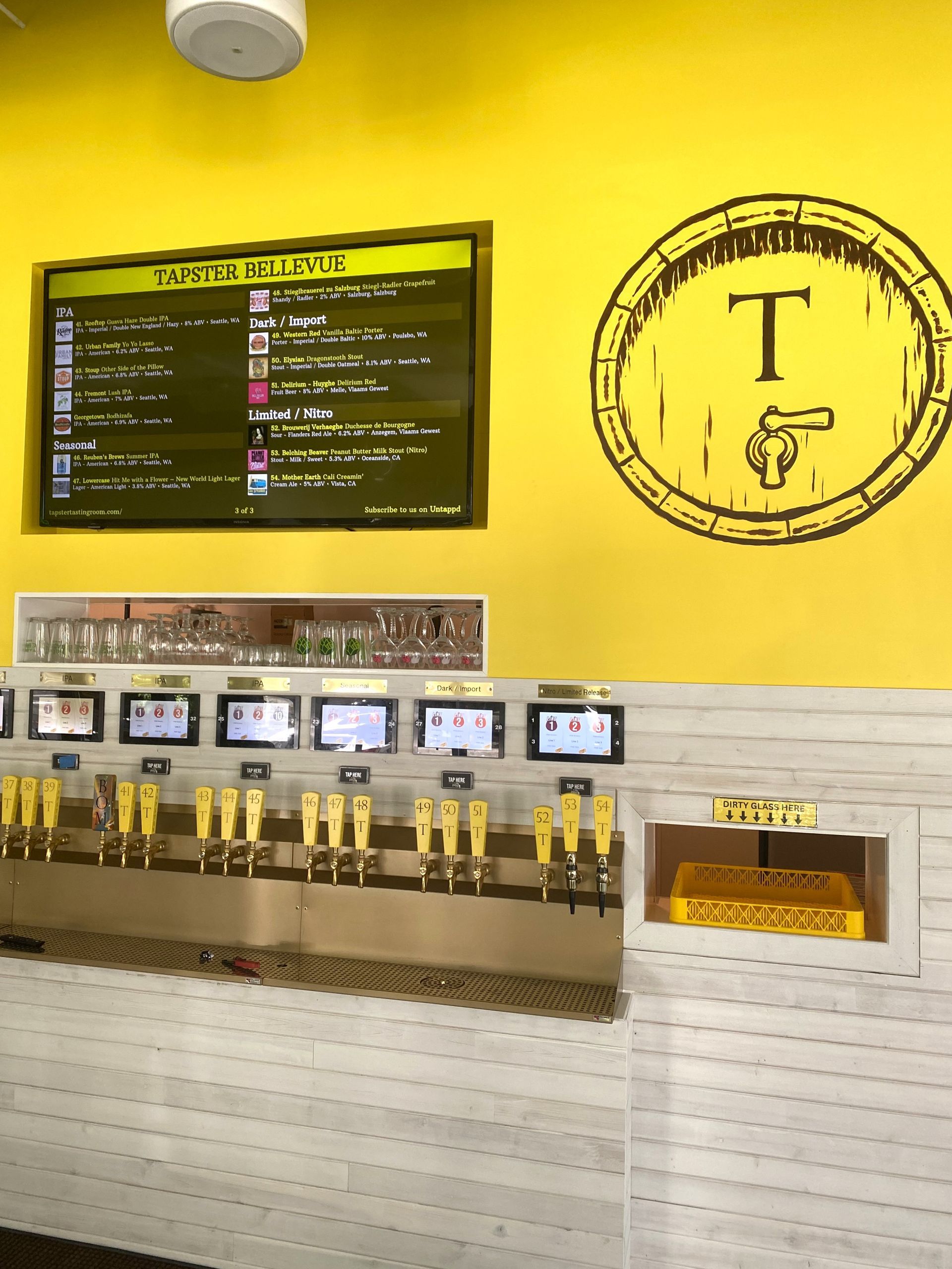 A bar with multiple taps on a yellow wall, a beer list, and a barrel logo.