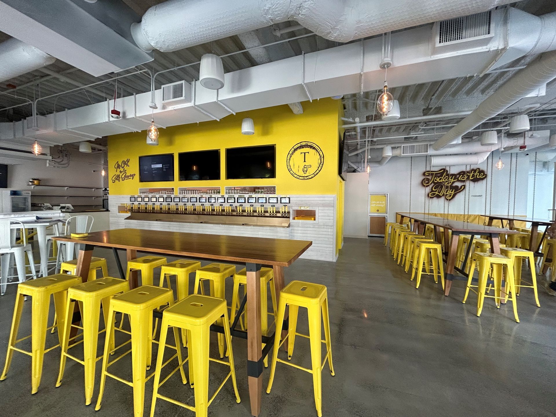 Interior of a brewery with a yellow and white color scheme. Yellow stools line tables in a spacious room.