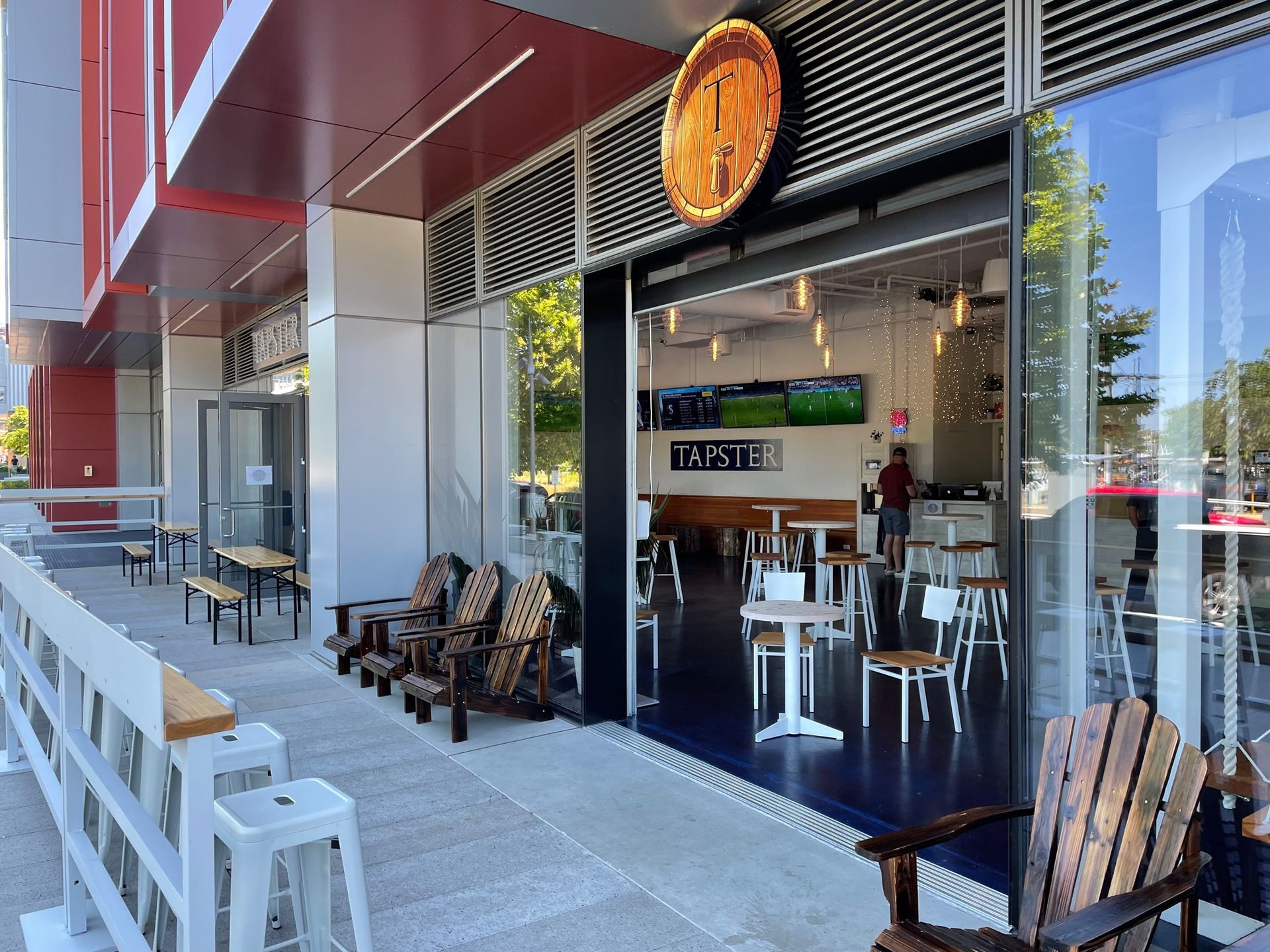 Exterior of a bar with open doors, patio seating, and a large sign above the entrance.
