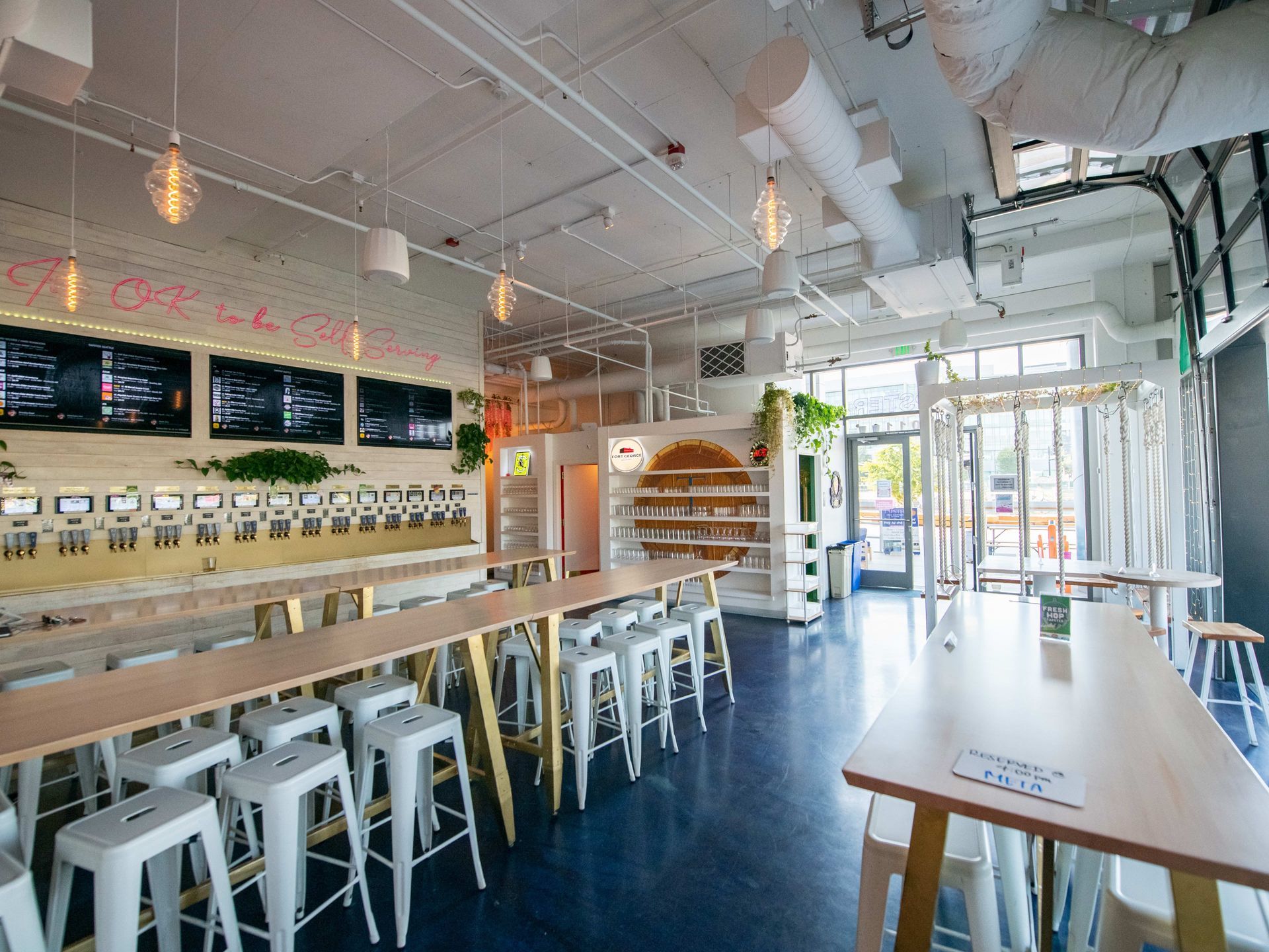 Bright, modern cafe interior with long tables, white stools, and a blue floor.