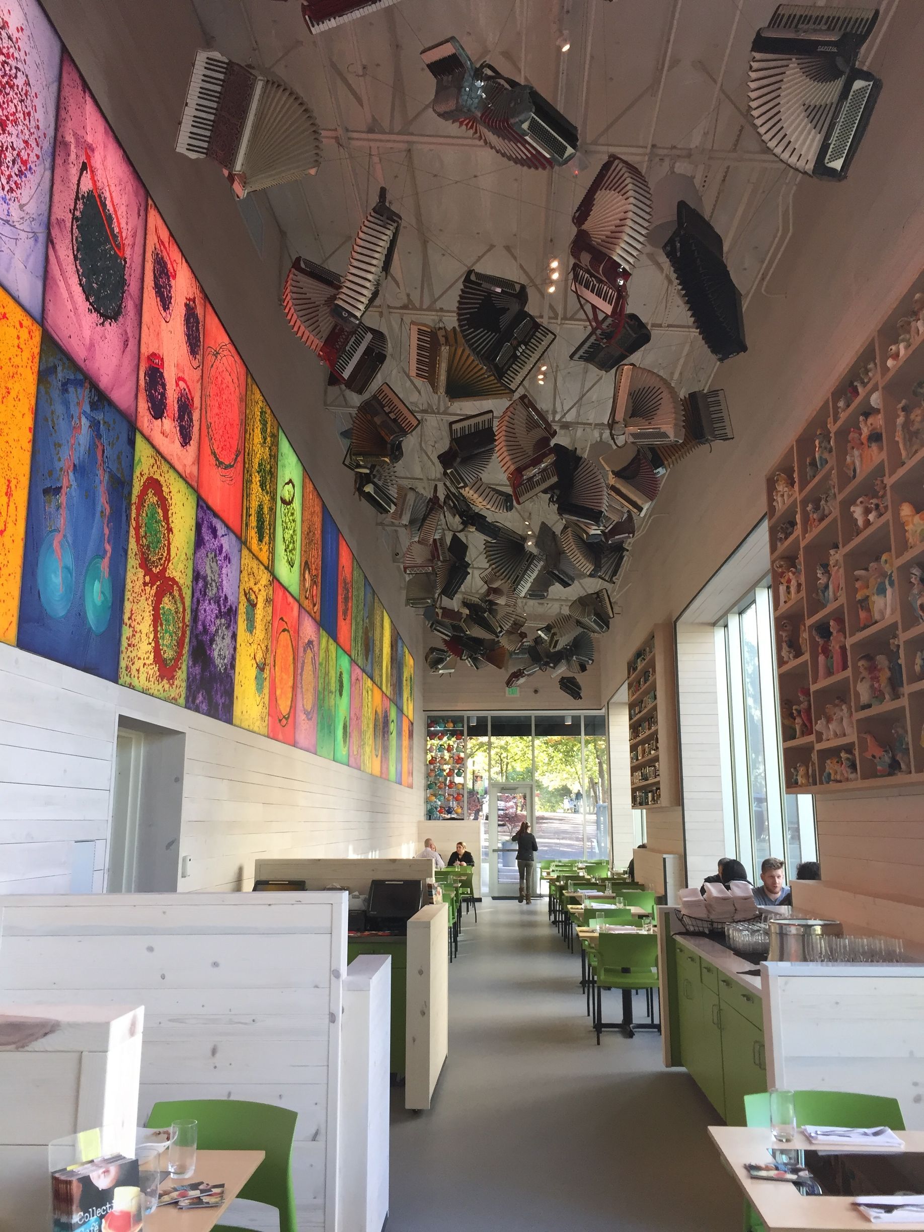 Restaurant interior with colorful wall art, accordions suspended from the ceiling, and tables with green chairs.