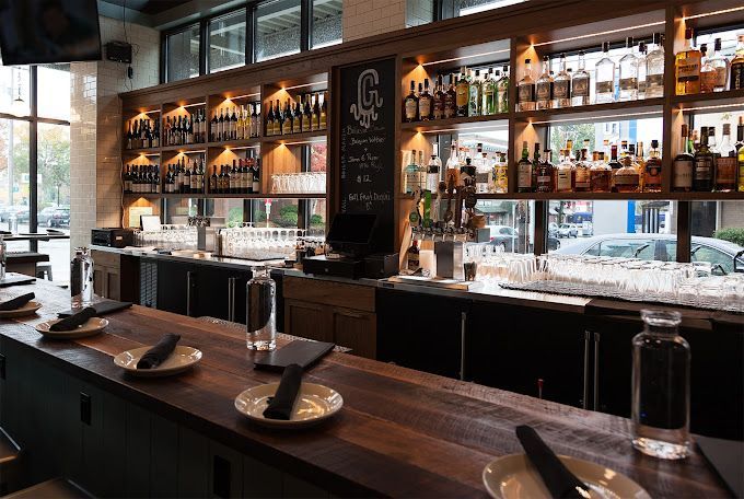 Bar interior with wooden bar top, shelves of liquor bottles, and tap handles.