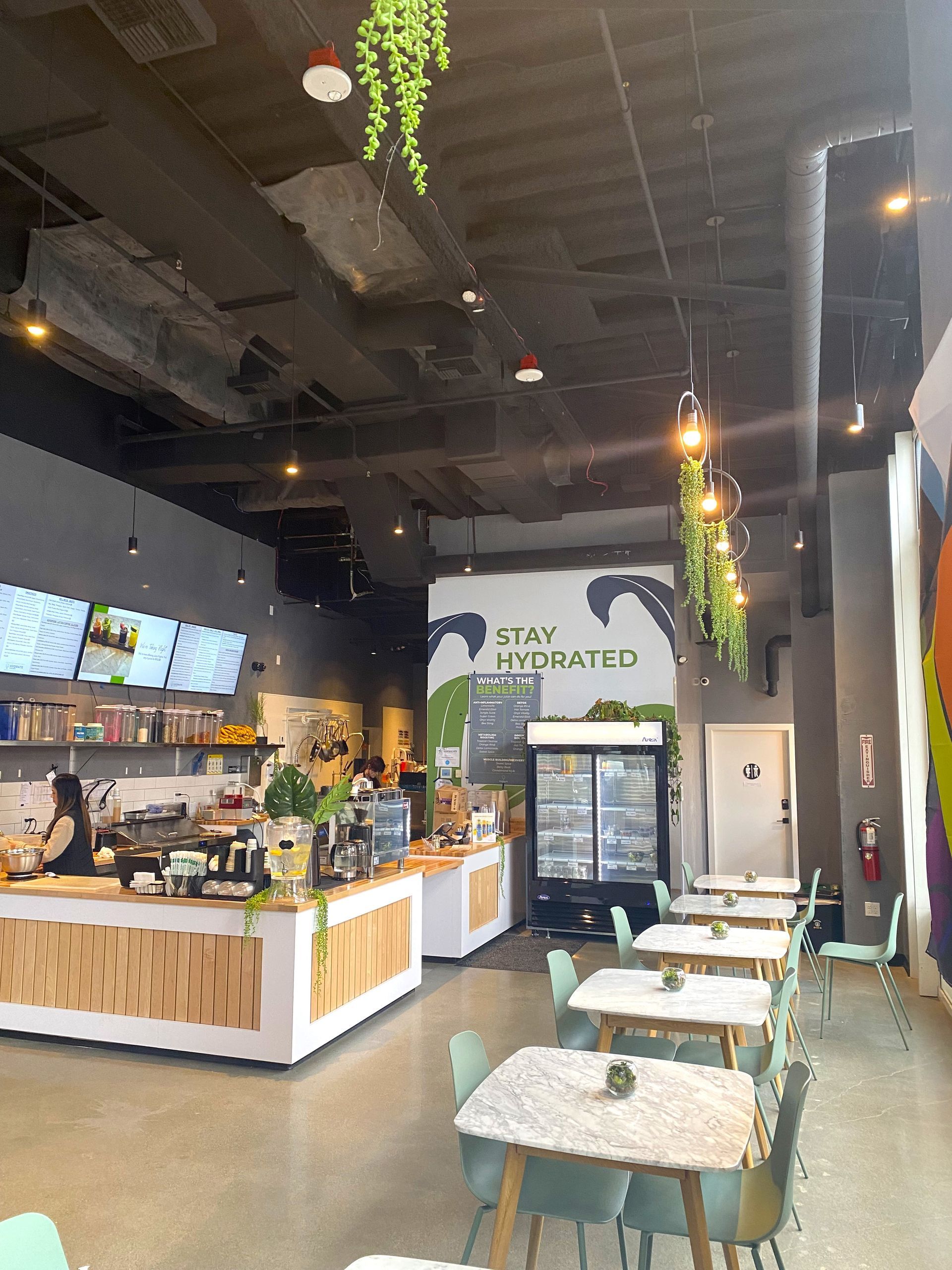 Interior of a cafe with tables and counter. A person works behind the counter. Green, white, and gray color scheme.