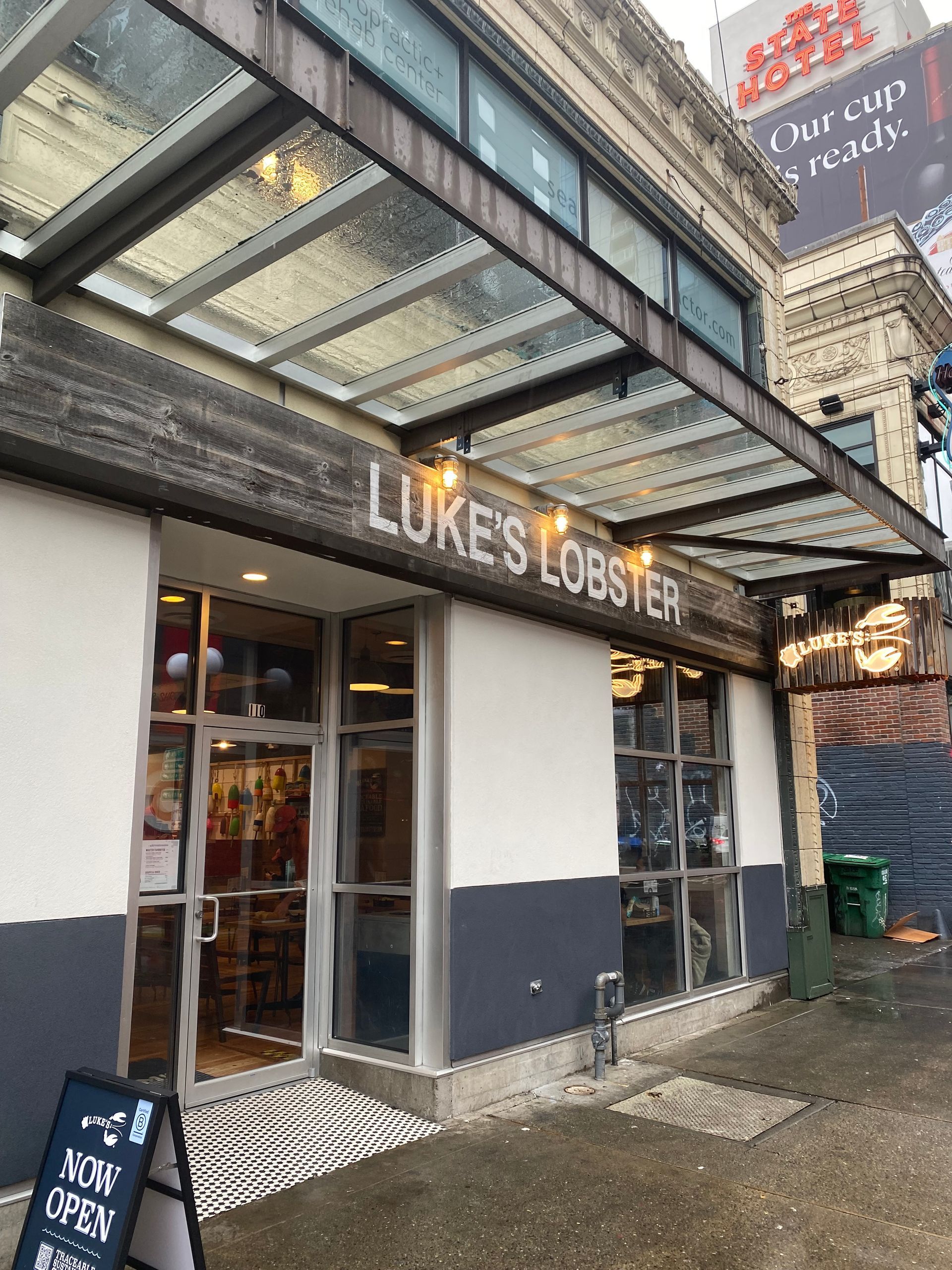 Luke's Lobster restaurant exterior with glass awning. The entrance has a sign and door with an open sign.